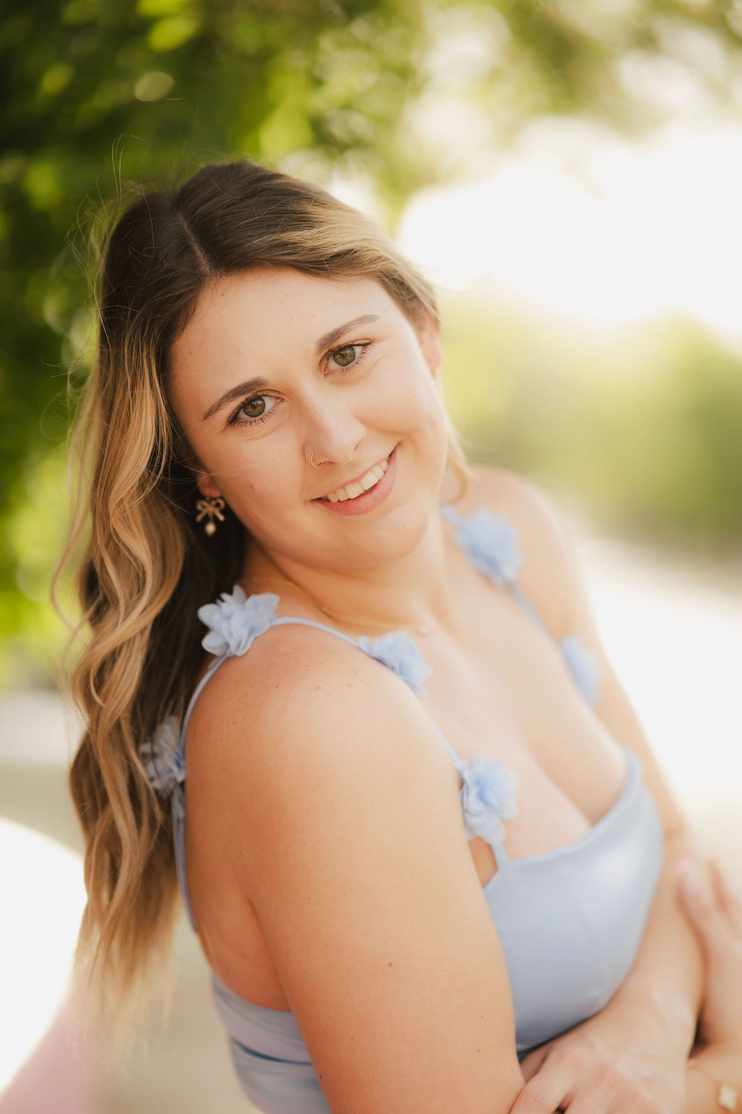 Smiling young woman in light blue floral dress with golden hour bokeh background.