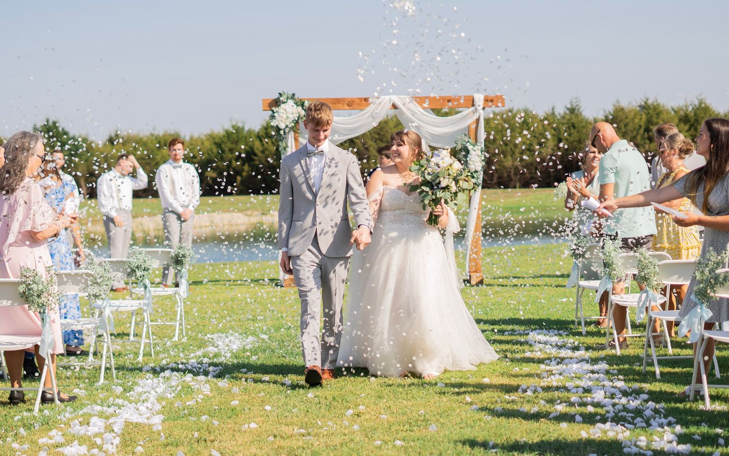 Bride and groom walking through petal toss at outdoor farm wedding ceremony.