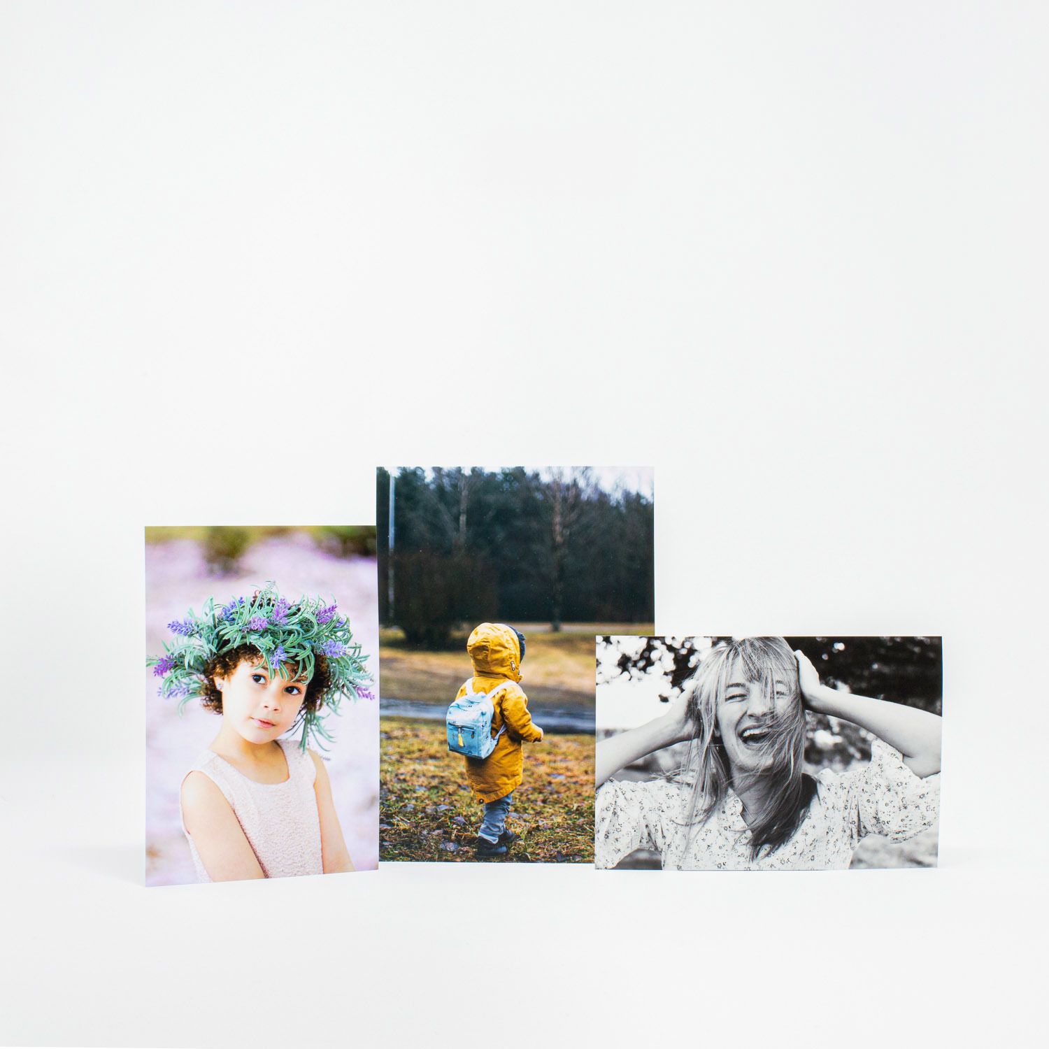 Three printed photos displayed standing up showing a child with flower crown, toddler outdoors, and laughing woman.