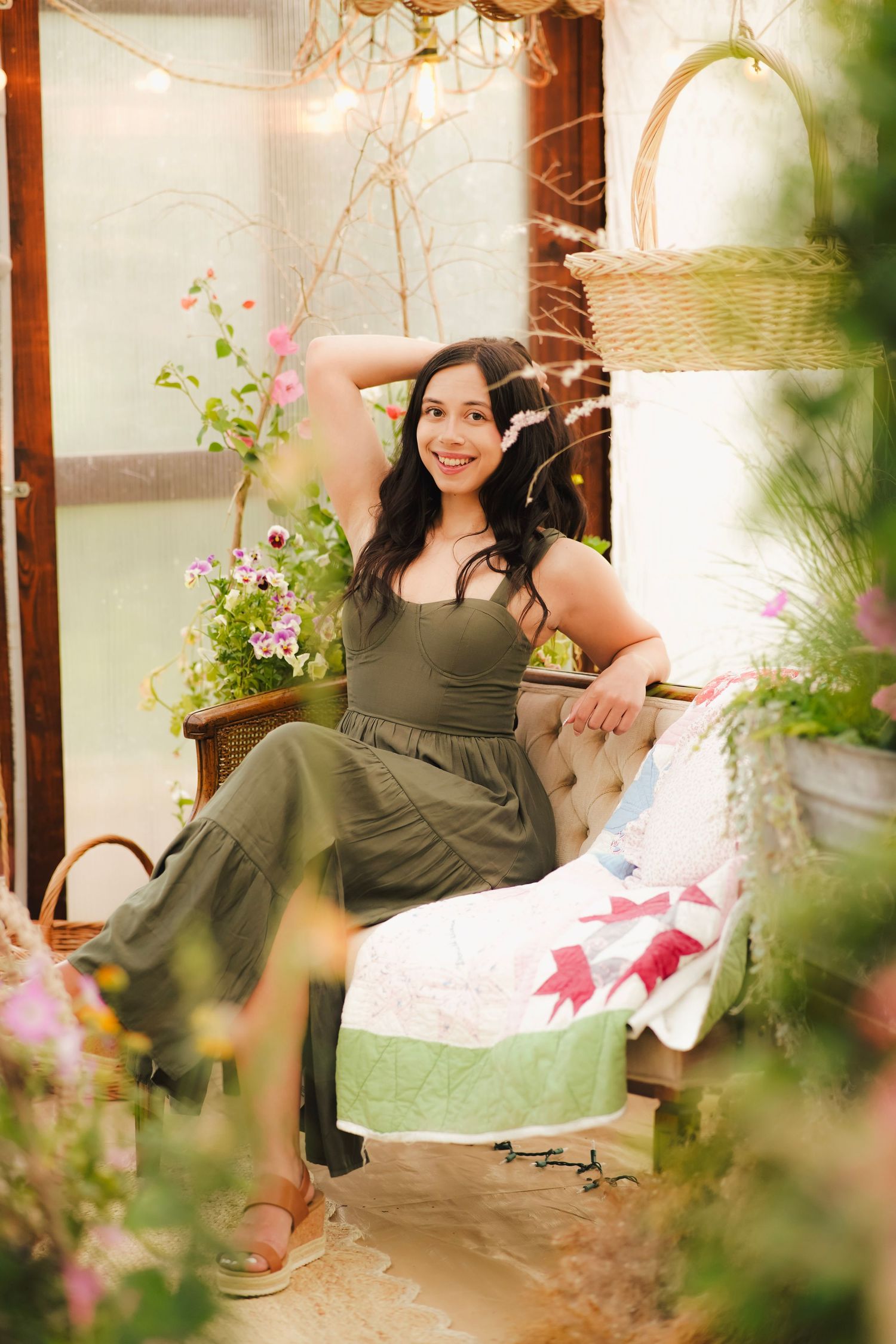Smiling woman in green dress relaxing on bench surrounded by flowers in greenhouse.
