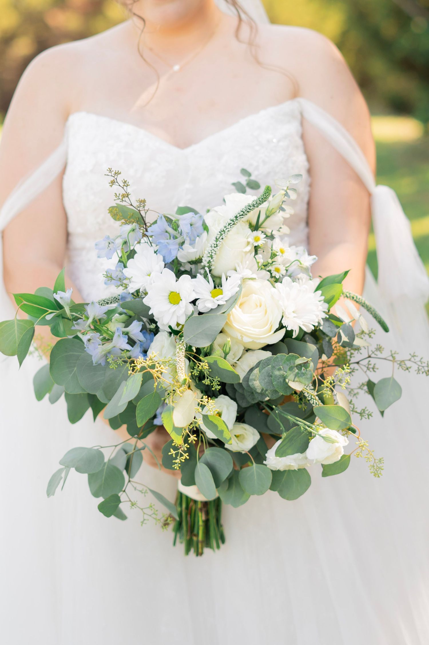 Bride holding loose white and blue wedding bouquet with eucalyptus greenery and daisies.