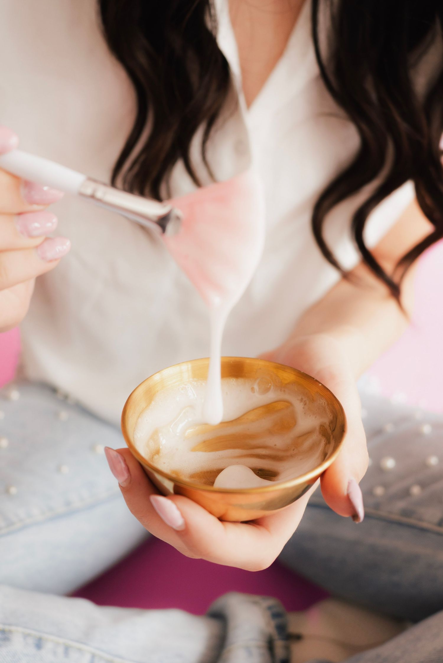 Woman pouring steamed milk into a golden bowl cup of latte art coffee with manicured hands.