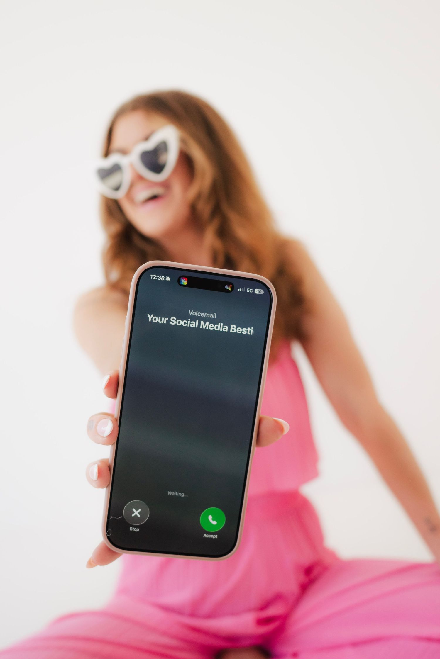 Smiling woman in pink outfit holding phone showing incoming call from Your Social Media Besti.