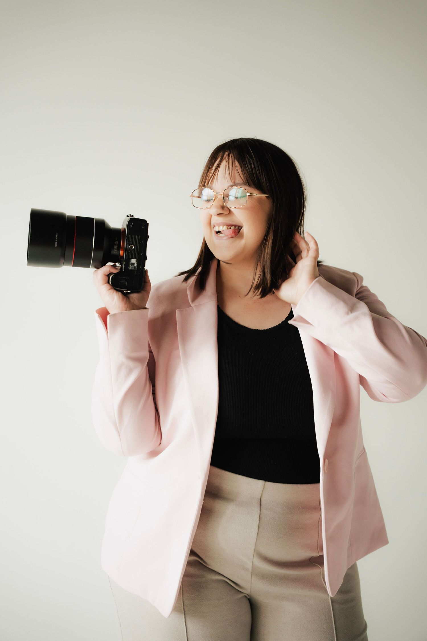 Playful female photographer in pink blazer making funny face while holding professional camera.