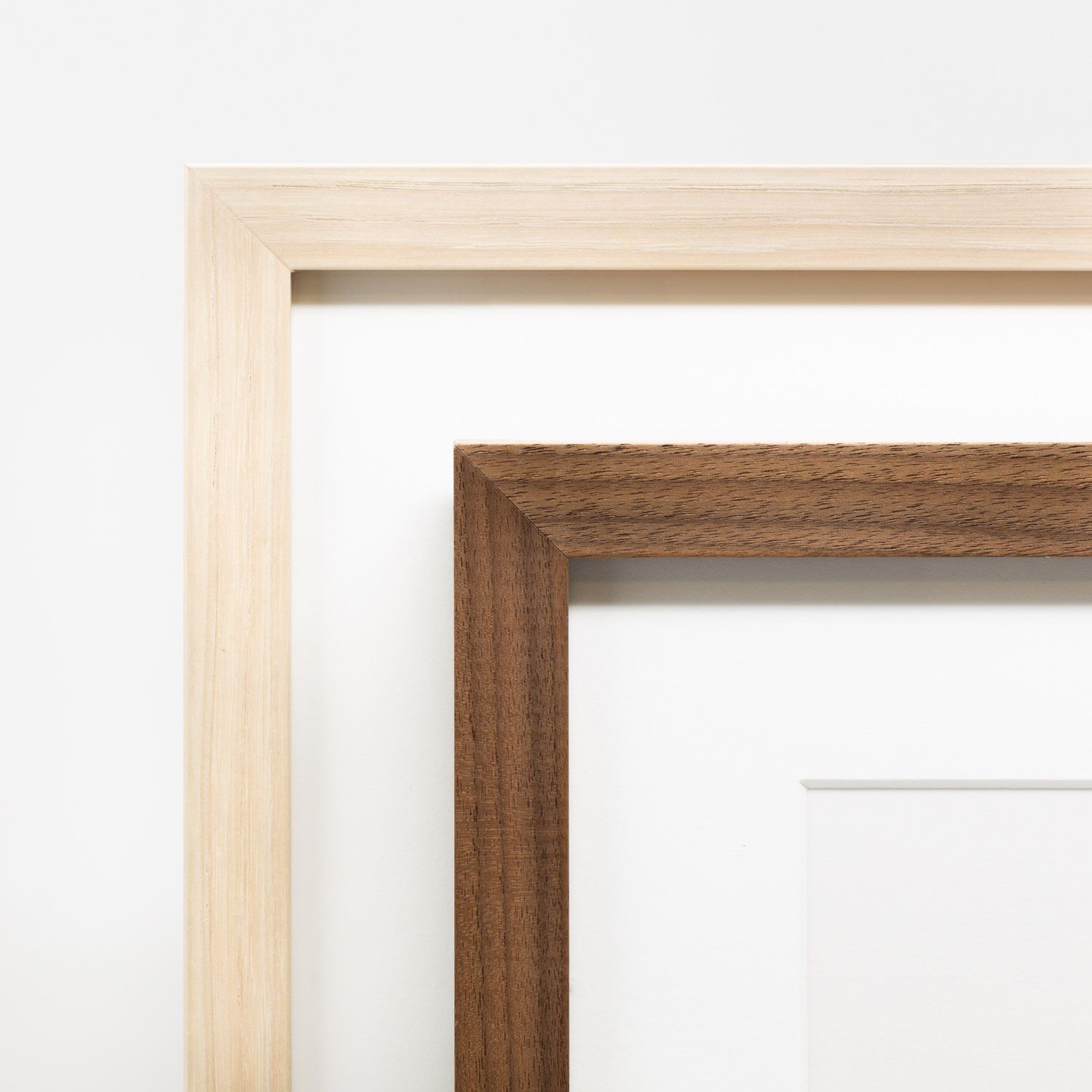 Two wooden picture frames in light maple and dark walnut finishes leaning against a white wall.