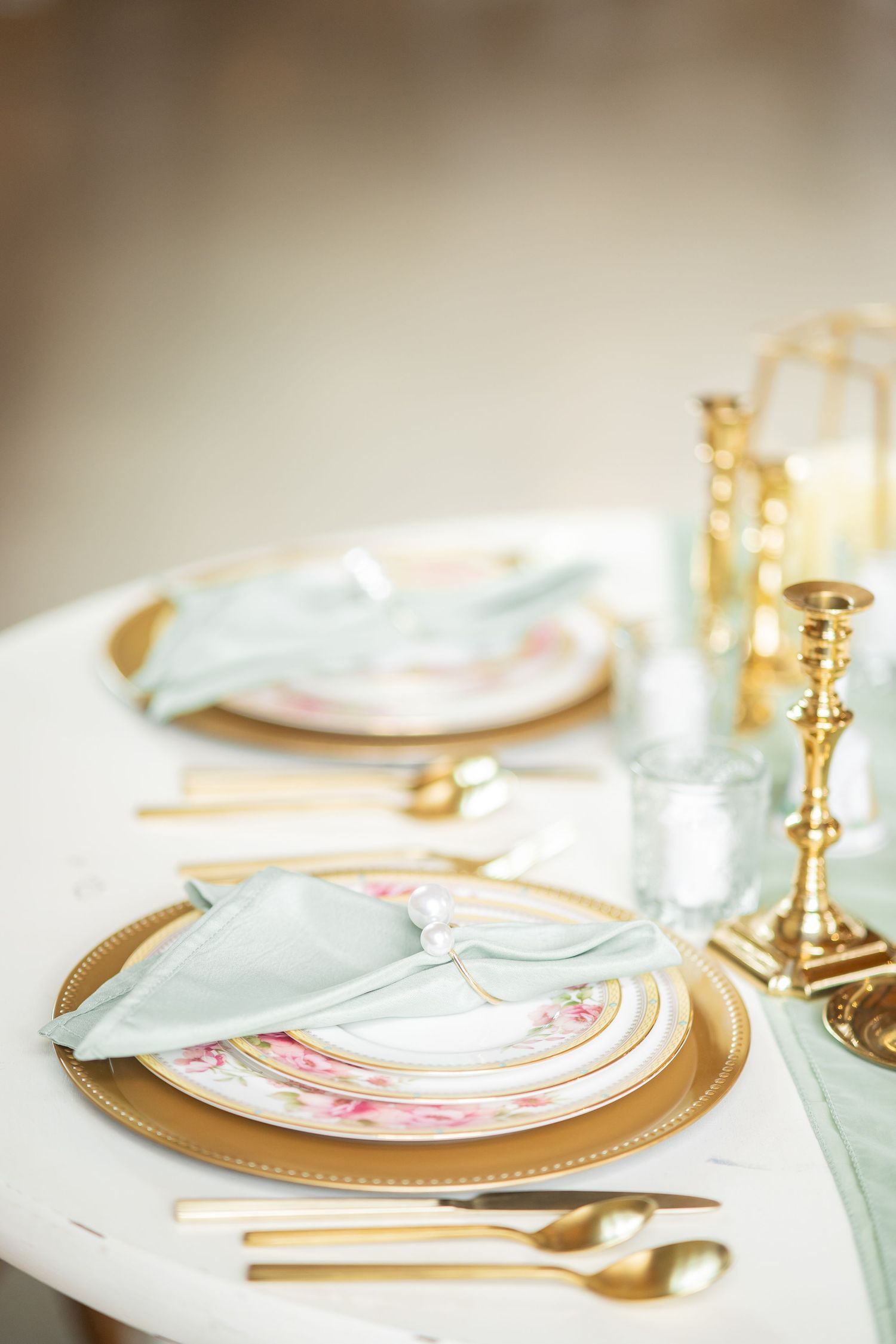 Elegant wedding table setting with gold chargers, floral china, mint napkins, and gold candlesticks.