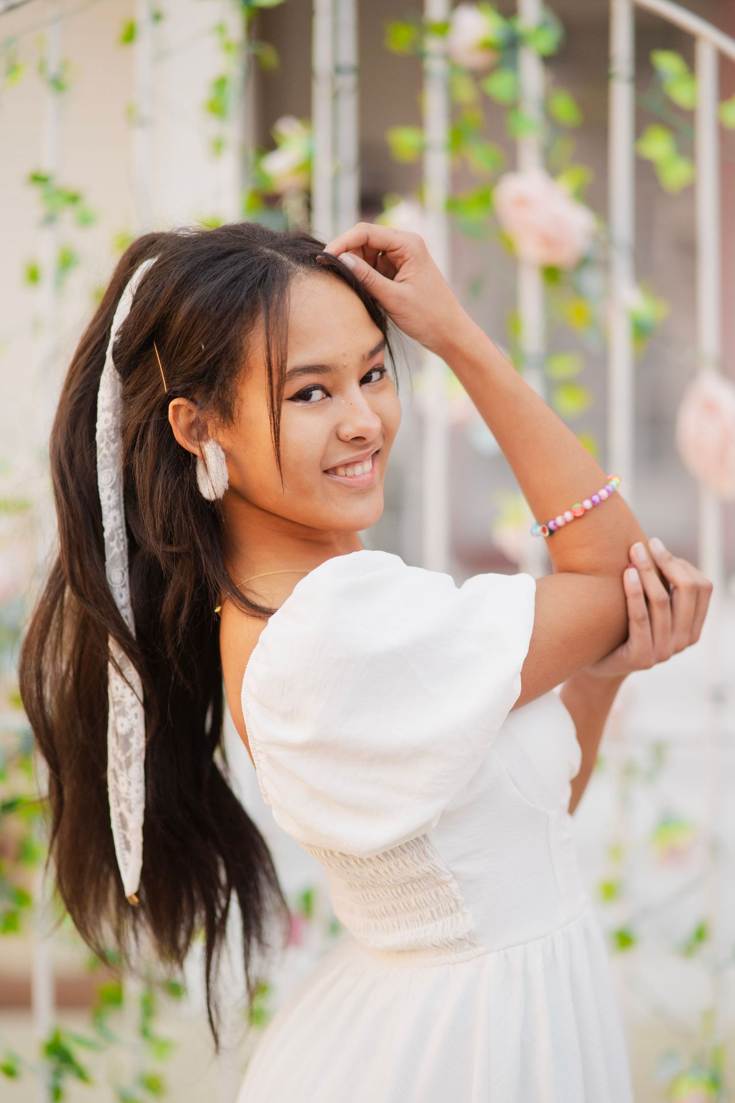 Smiling young Asian teen in white puff sleeve dress with hair accessory outdoors.