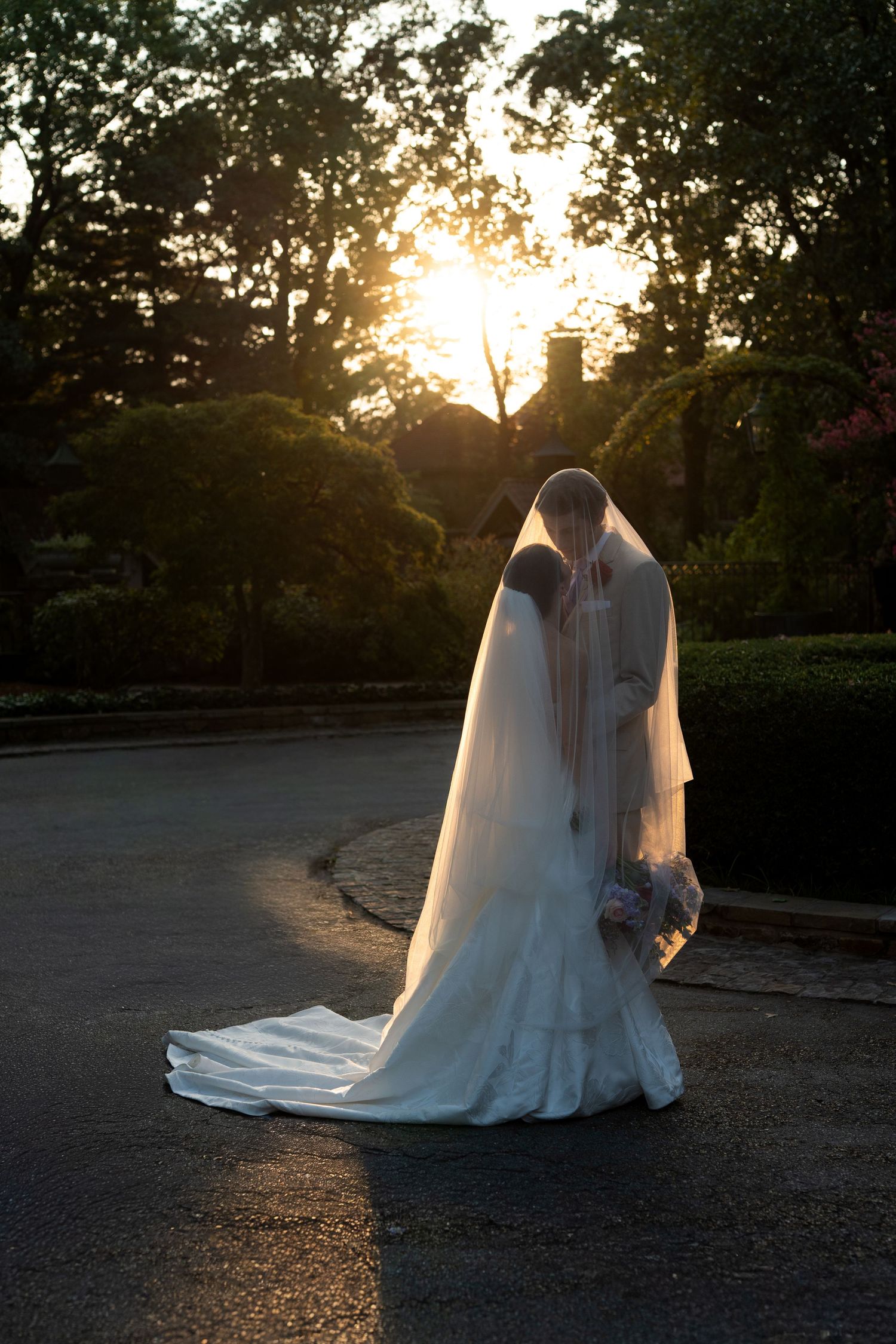 Wedding couple silhouetted against a sunset in a garden setting.