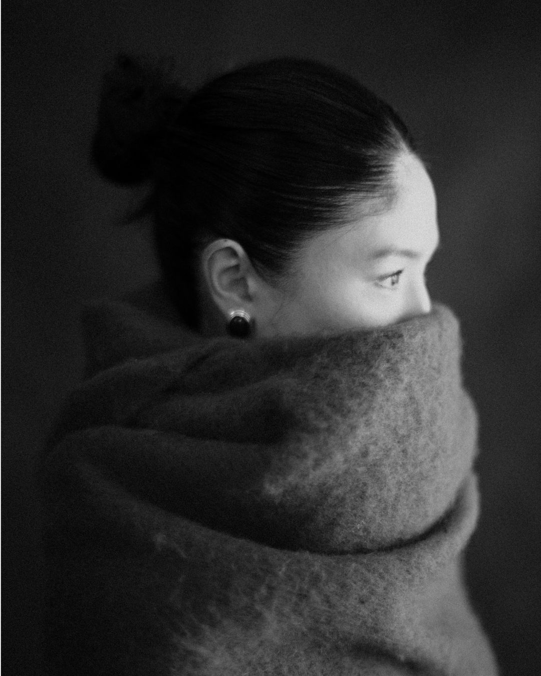 Black and white portrait of a woman wrapped in a cozy wool blanket, hair in a bun, wearing a stud earring.