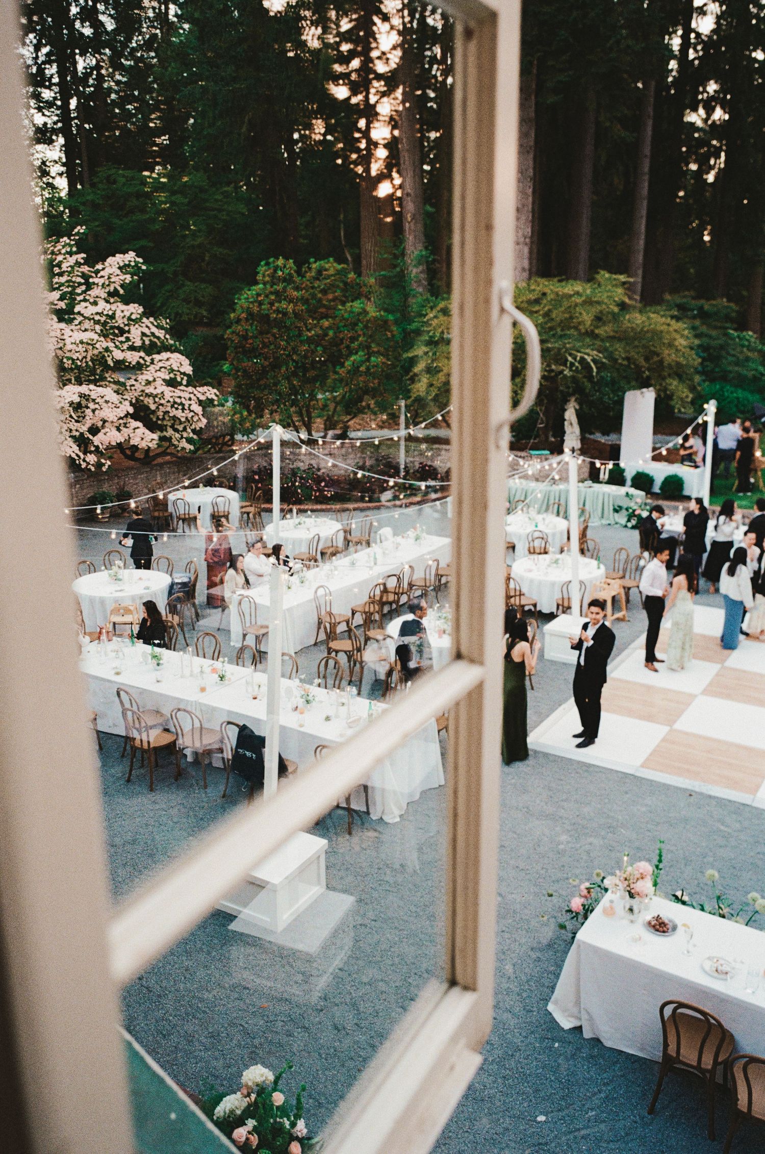 Aerial view of an elegant outdoor wedding reception with white tables, dance floor, and tall trees at dusk.