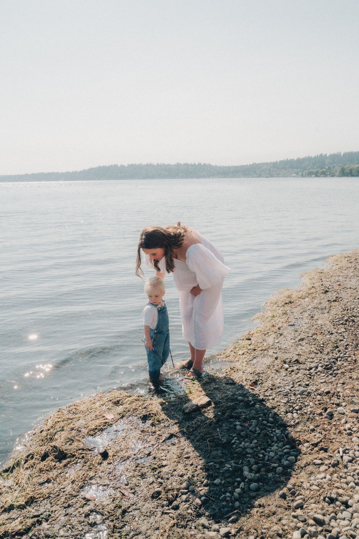 Two people explore a rocky beach shoreline on a sunny summer day while looking for treasures along the water's edge.
