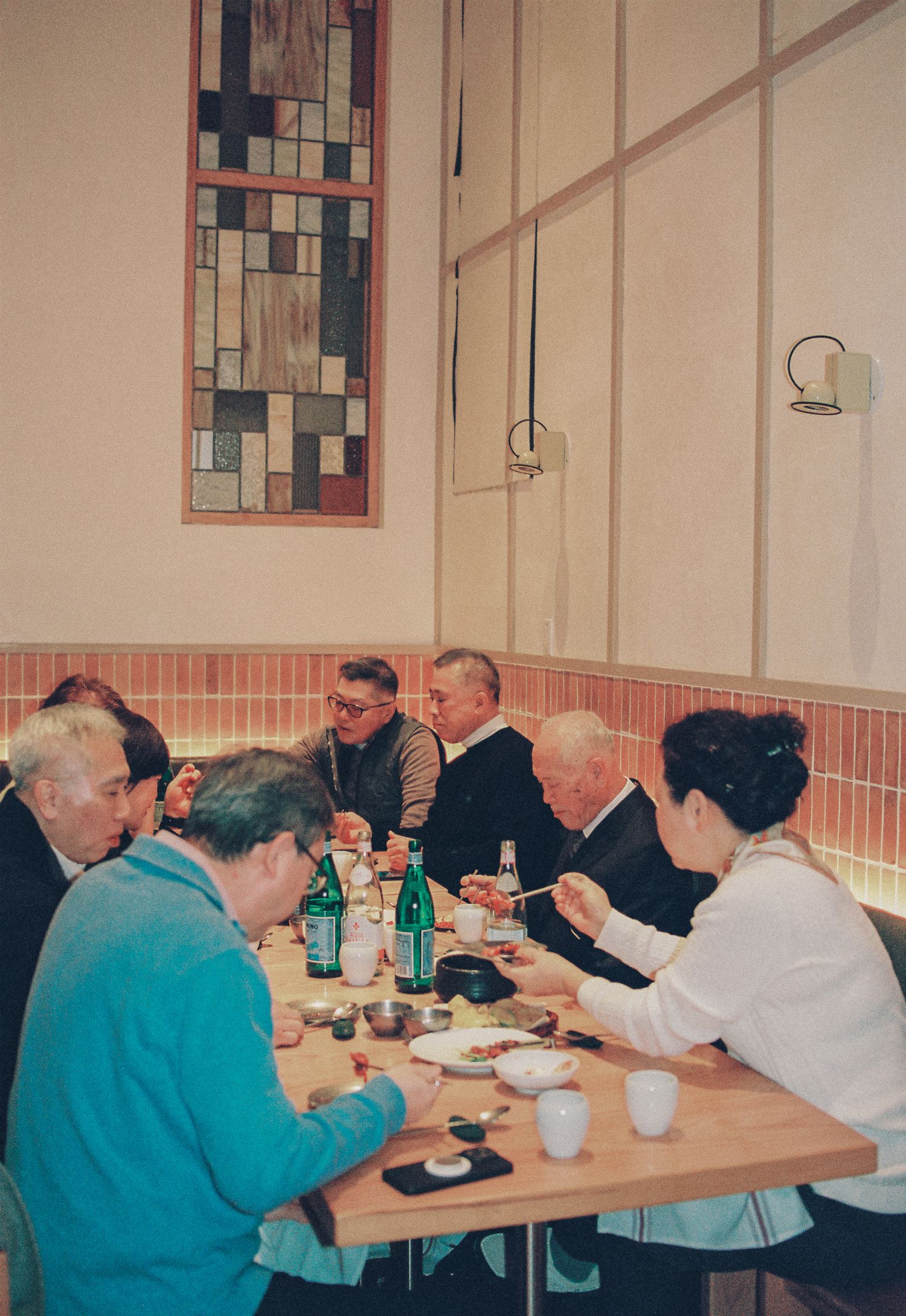 Group of people dining together at a restaurant table with drinks and dishes, seated in a cozy booth setting.