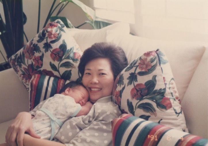 Person resting on white bedding with floral print pillows and decorative greenery in background.