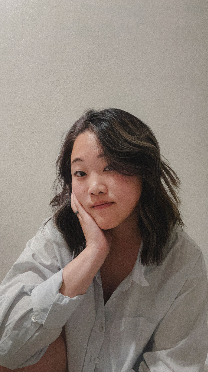 Portrait showing someone in casual white attire resting their face on their hand against a neutral wall.