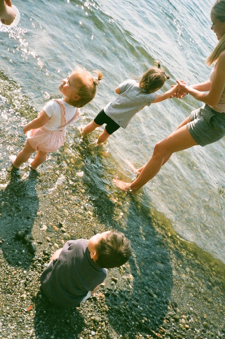 People enjoying a summer day splashing and playing in shallow water along a rocky shoreline.