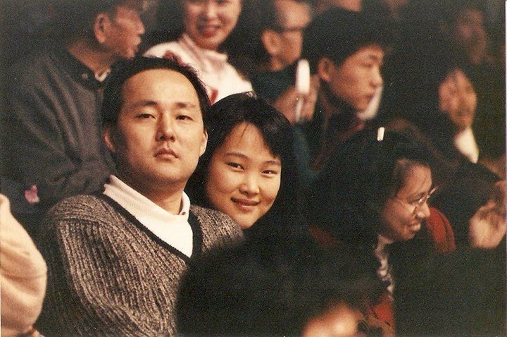 Three people sitting together in an audience wearing casual attire at what appears to be an indoor event.
