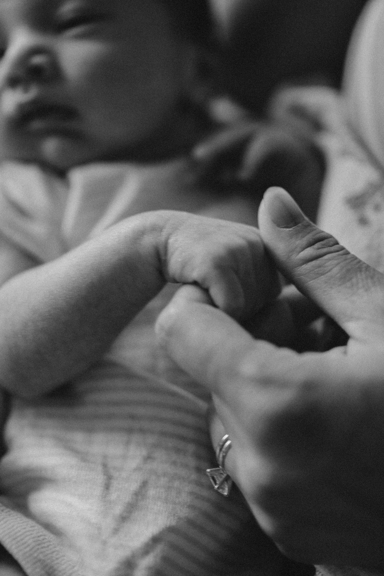 A tender black and white close-up of a baby's tiny hand being held by an adult wearing a ring.