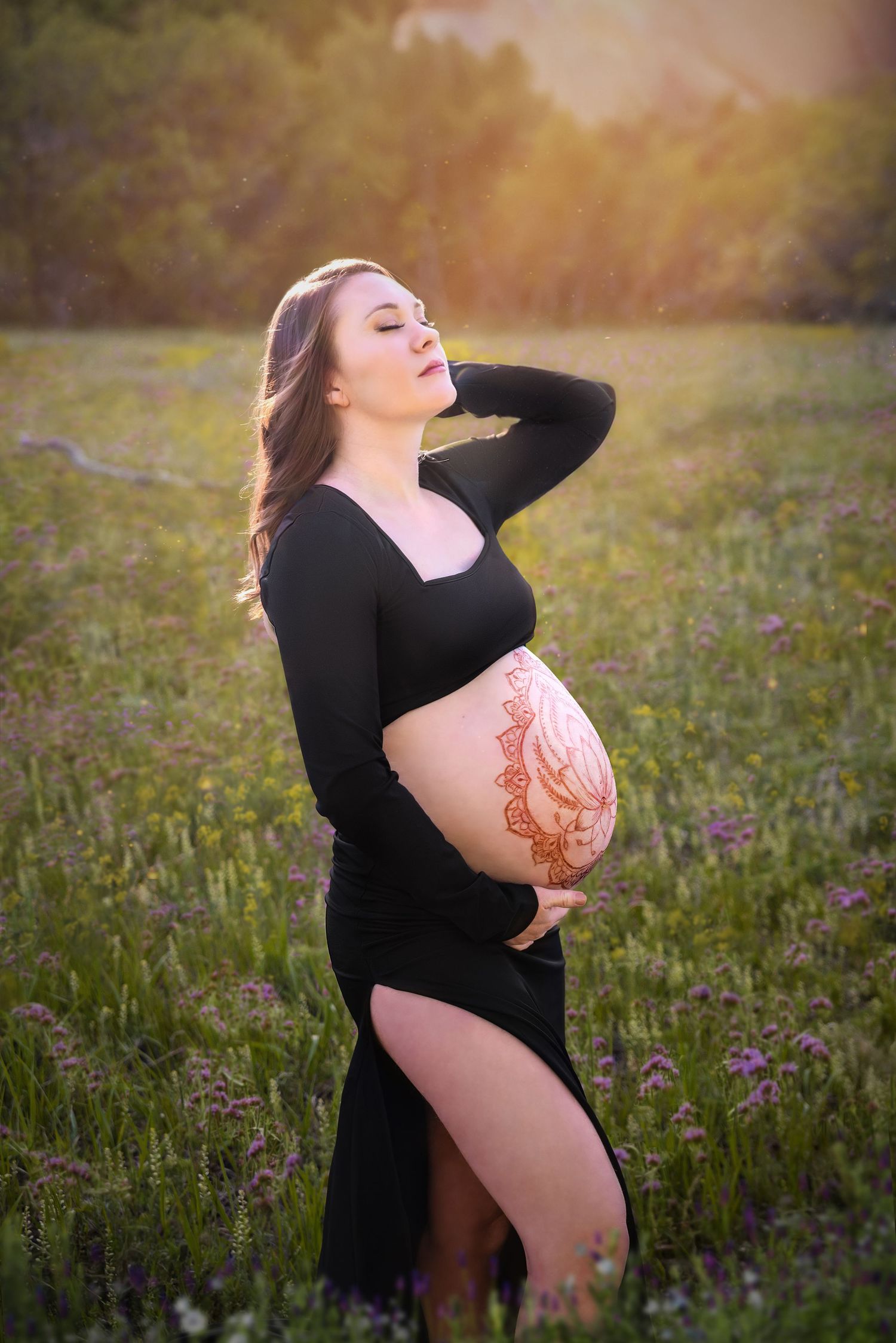 A fine art maternity portrait  of a woman in a black dress in a wildflower meadow at sunset taken by a photographer in Denver.