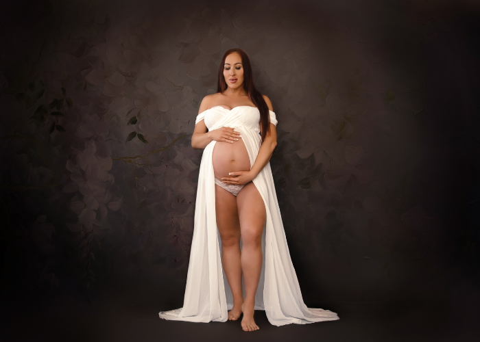 Elegant maternity portrait featuring flowing white fabric against a dark studio backdrop.