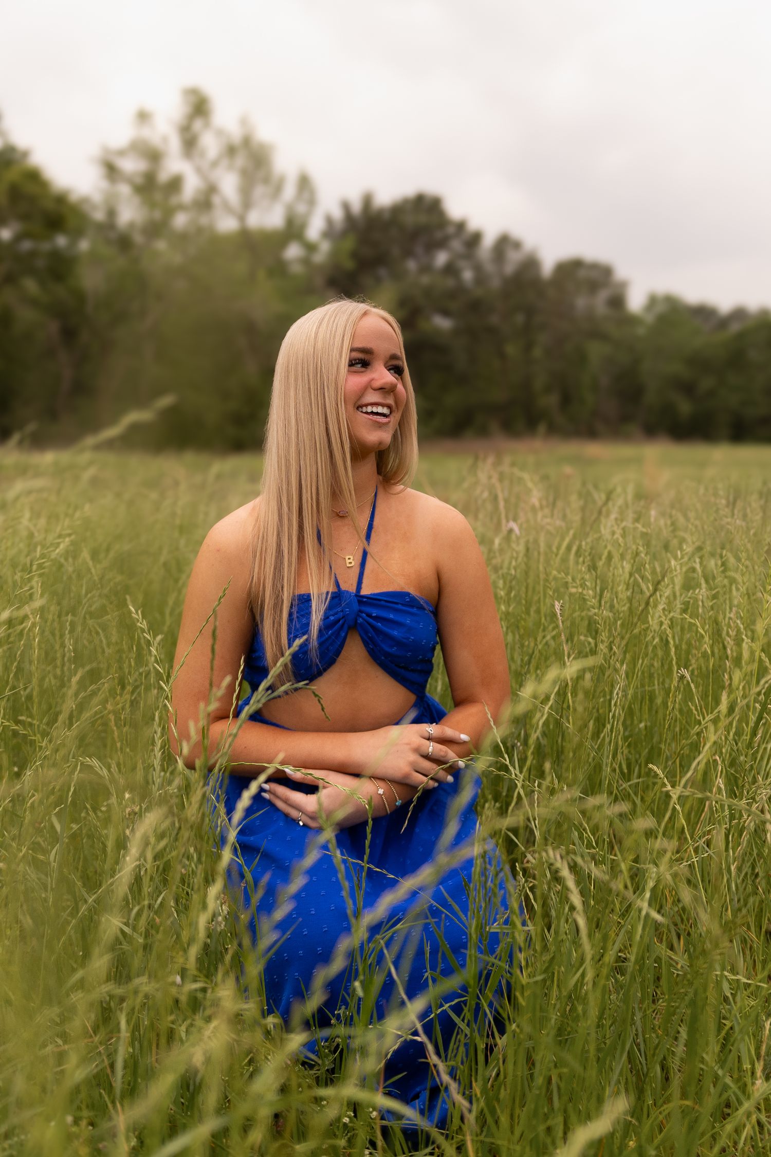 Laughing blonde woman in blue two-piece outfit standing in tall green grass.