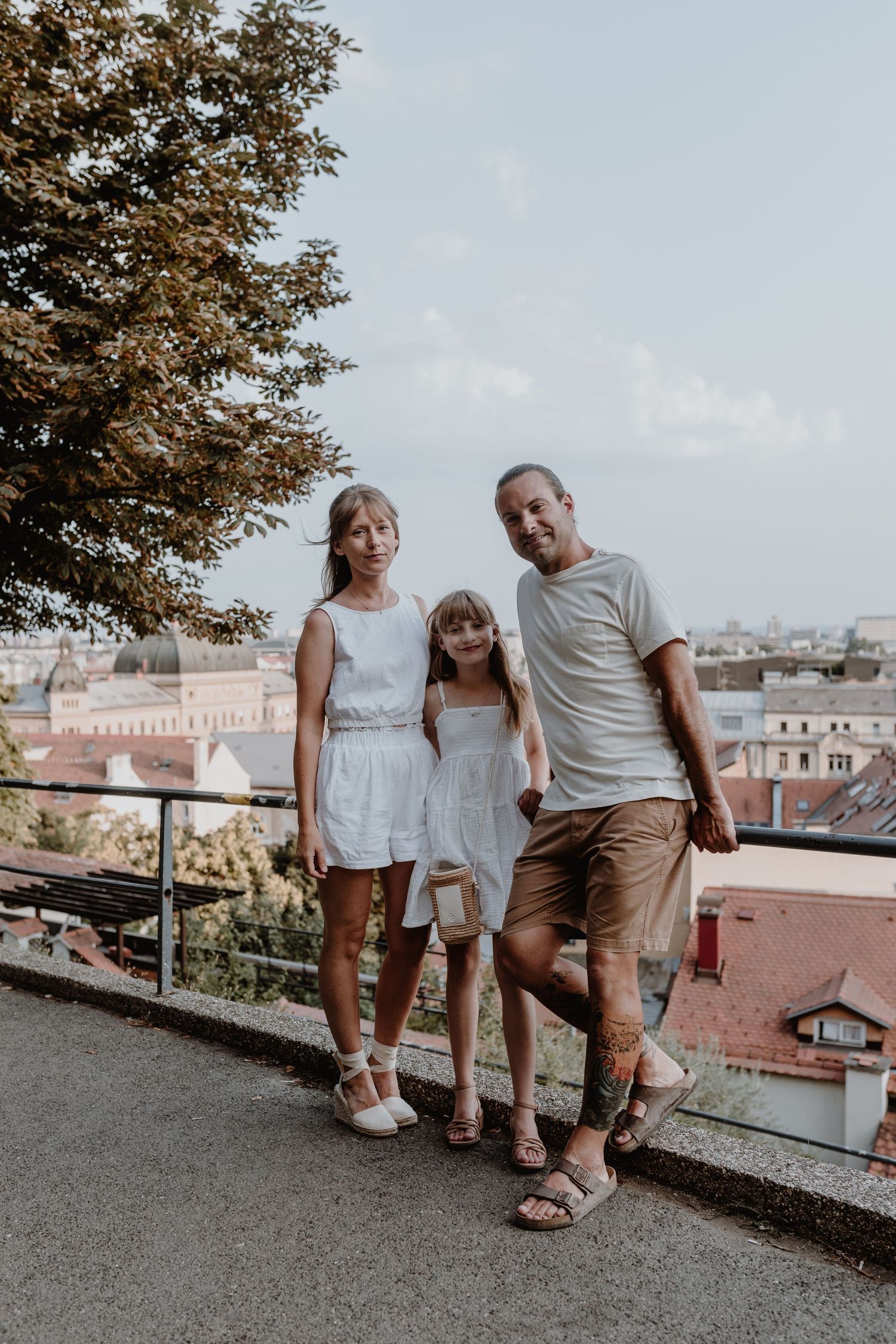 A family enjoys sightseeing at a scenic overlook with red rooftops and city buildings visible in the background.