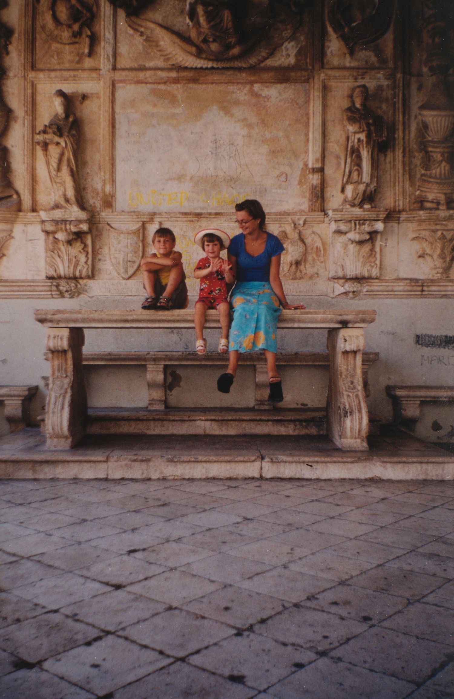Family resting on a decorative stone bench in a historic courtyard setting.