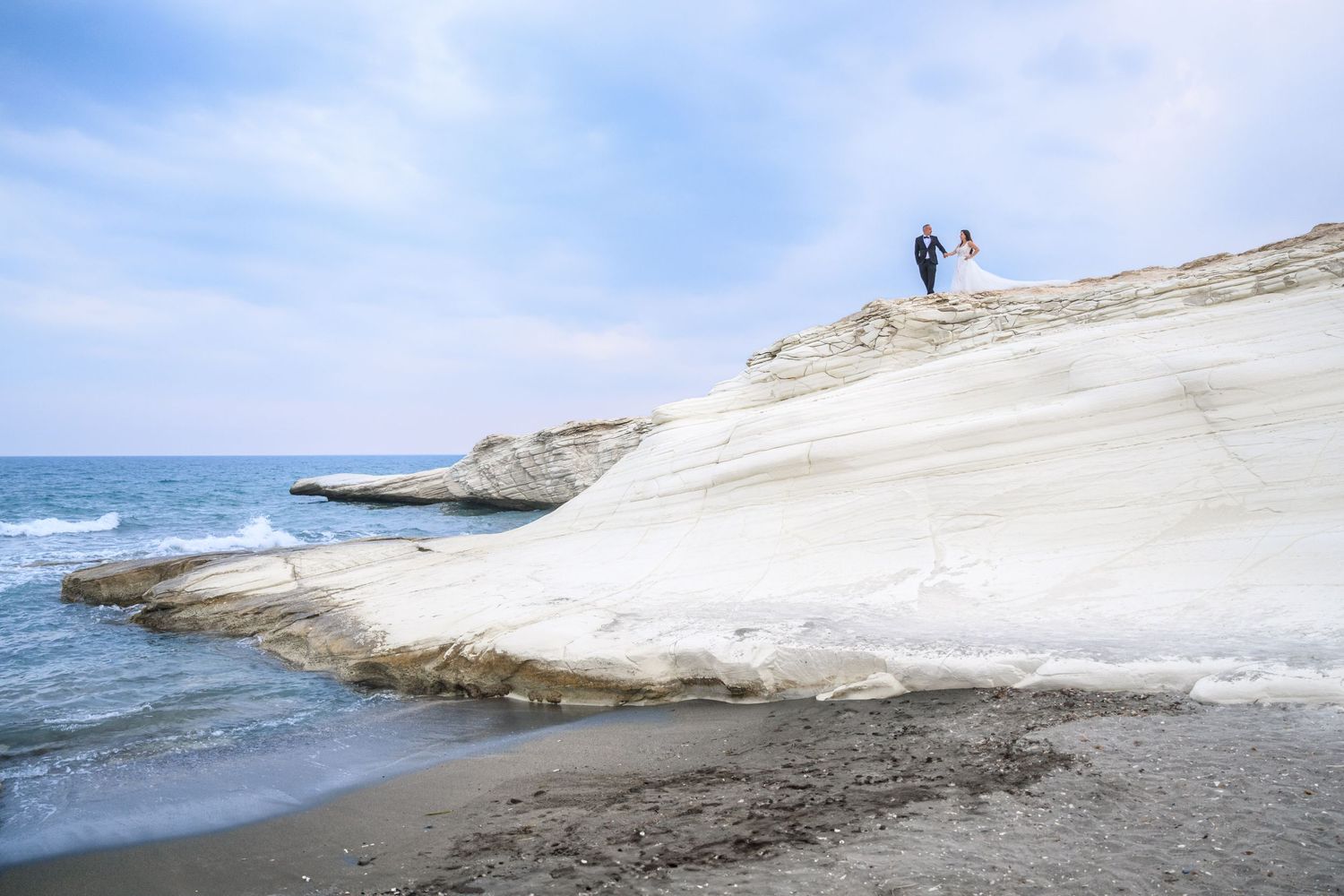 A couple stands on the white limestone cliffs of Scala dei Turchi in Sicily overlooking the Mediterranean Sea.