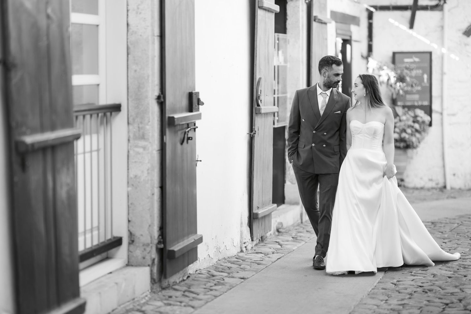 A romantic black and white wedding photo of a couple walking down a charming cobblestone street.