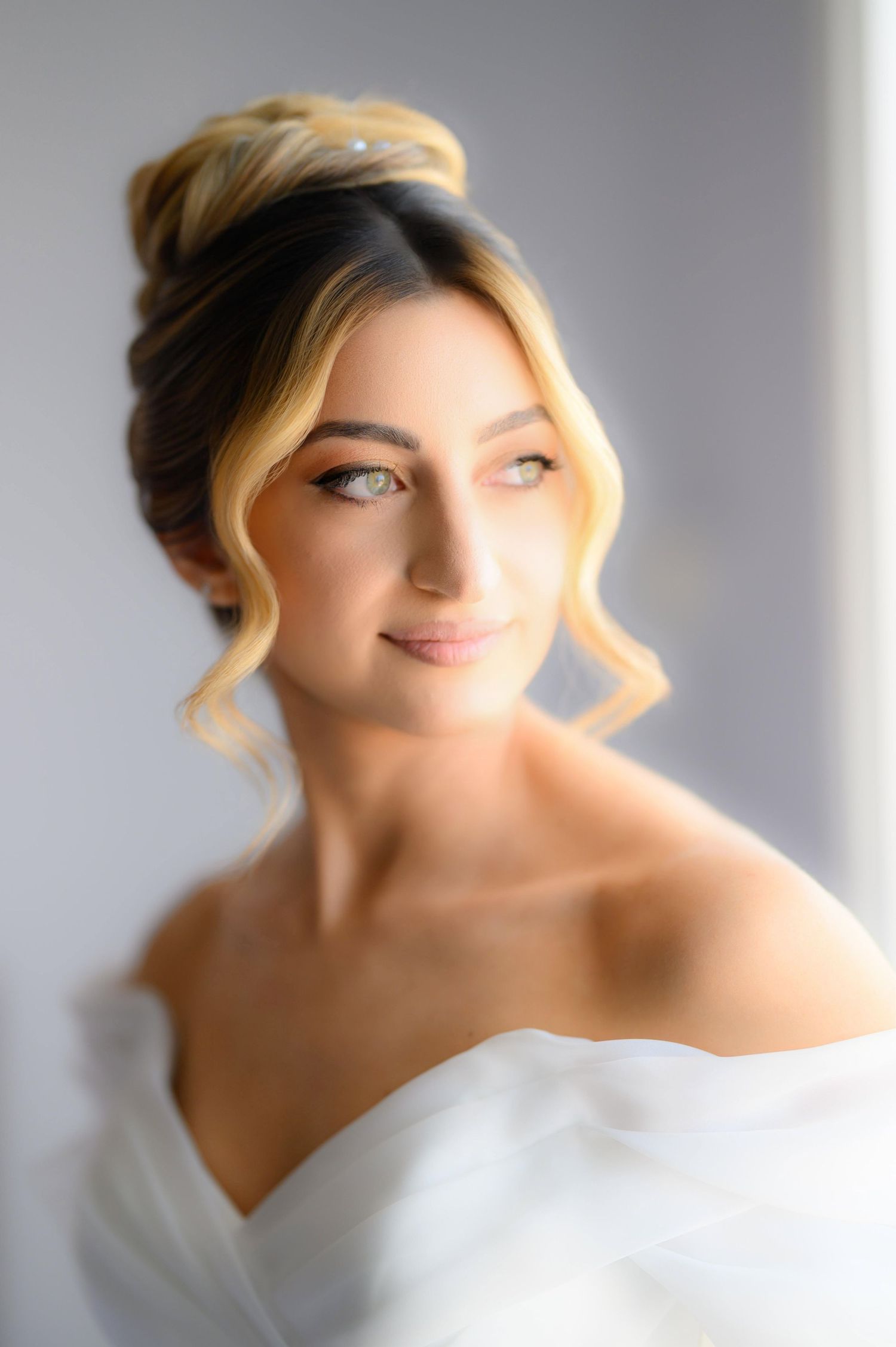 Close-up portrait of a bride in a white off-shoulder dress with soft romantic styling and glowing natural makeup.