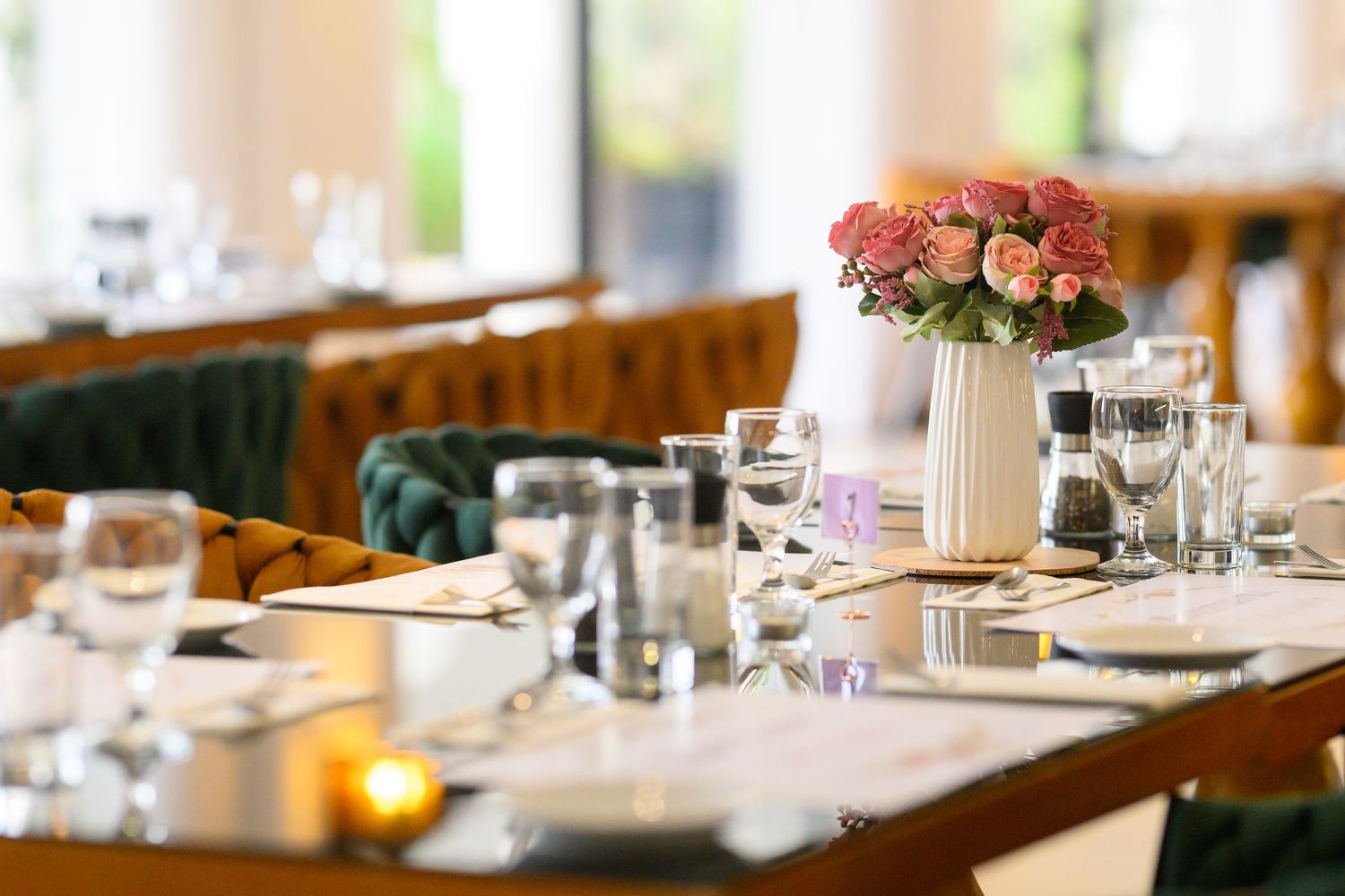 Elegant table setting in a restaurant with pink flowers in white vase, glassware and natural lighting.
