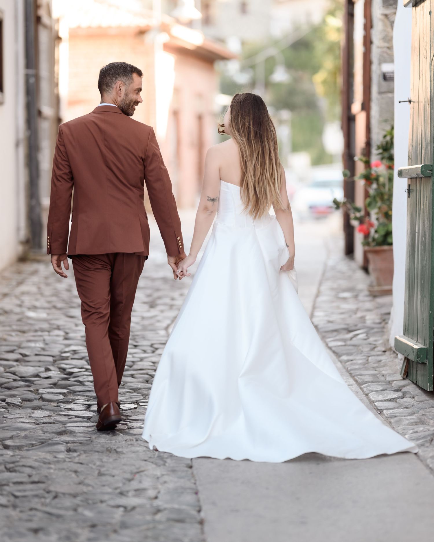 Newlyweds walking down a cobblestone street in wedding attire.
