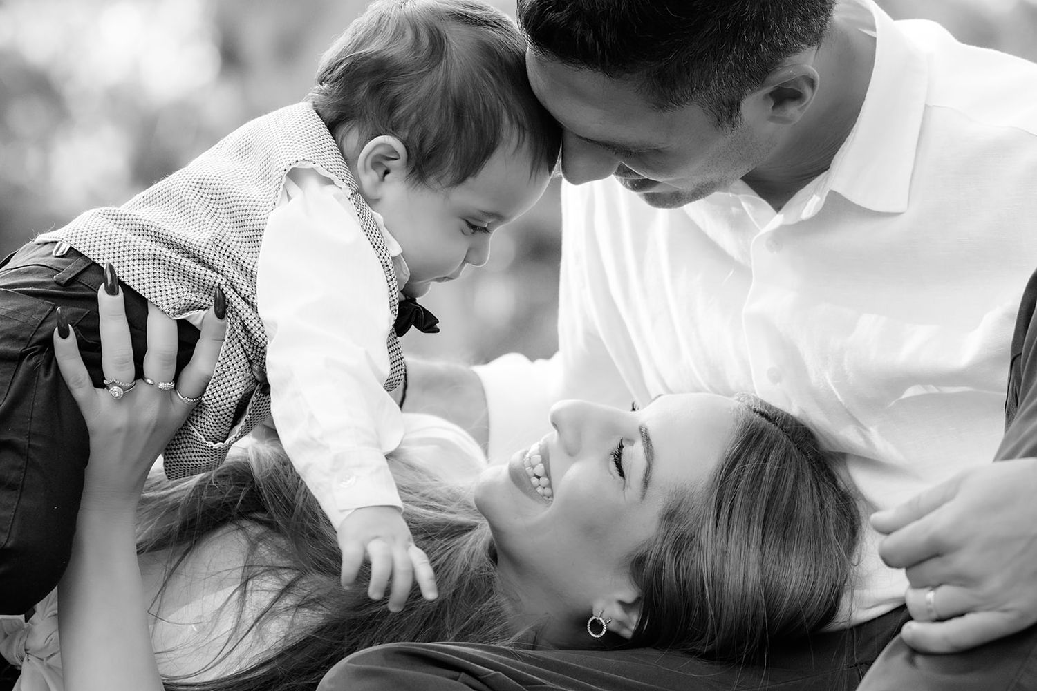 Black and white intimate family portrait showing tender moment of parents playing with their young child while laying down.