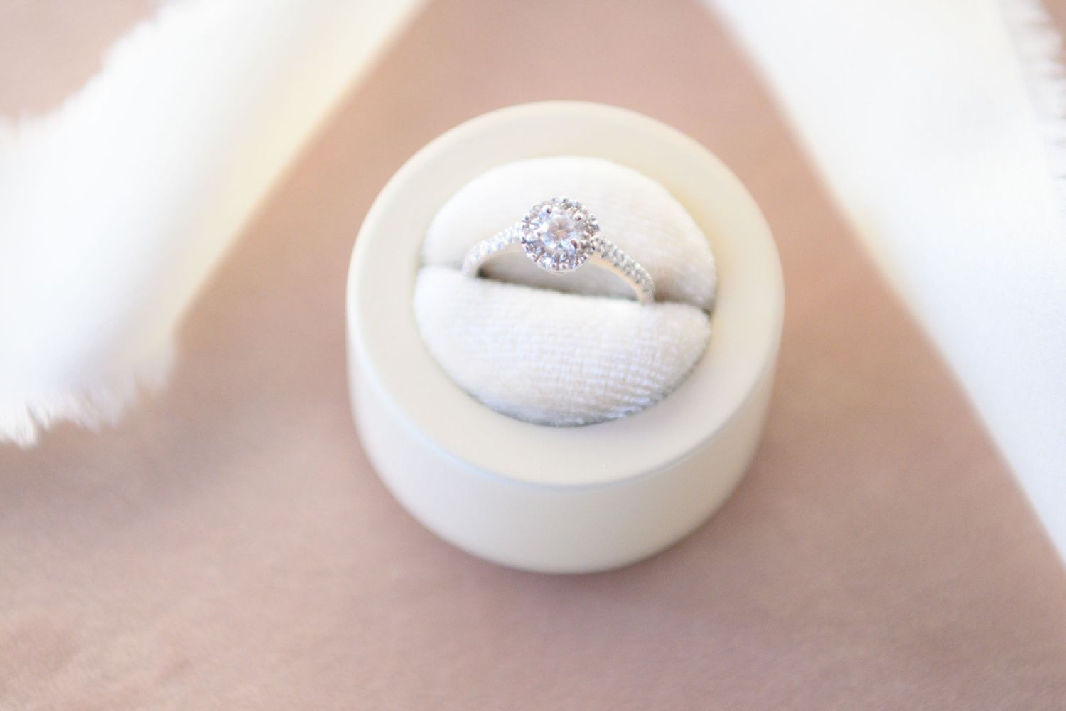 A white round engagement ring box with a sparkling diamond ring nestled inside.