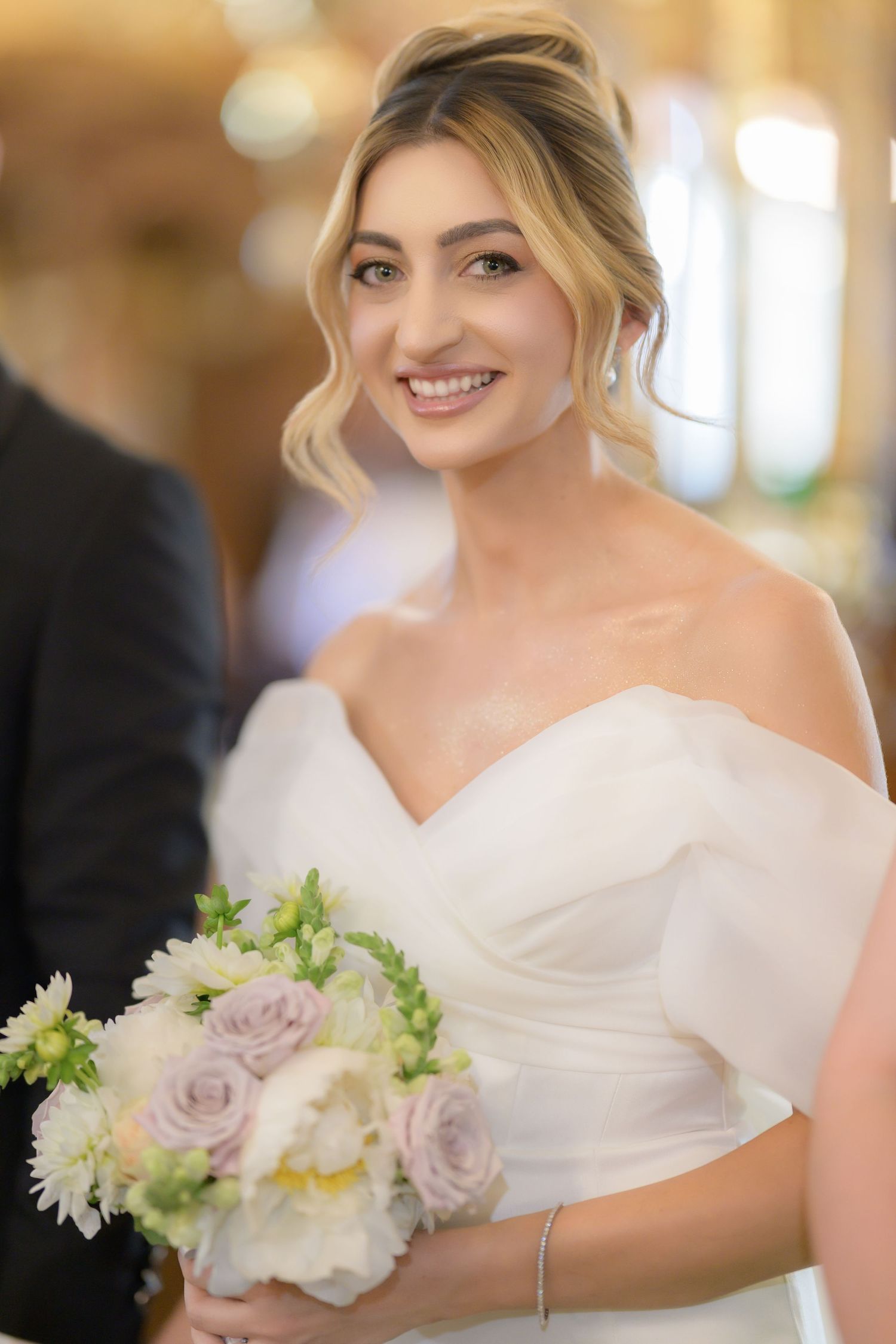 A bride in a classic white wedding dress holds a delicate bouquet of lavender roses and white daisies.