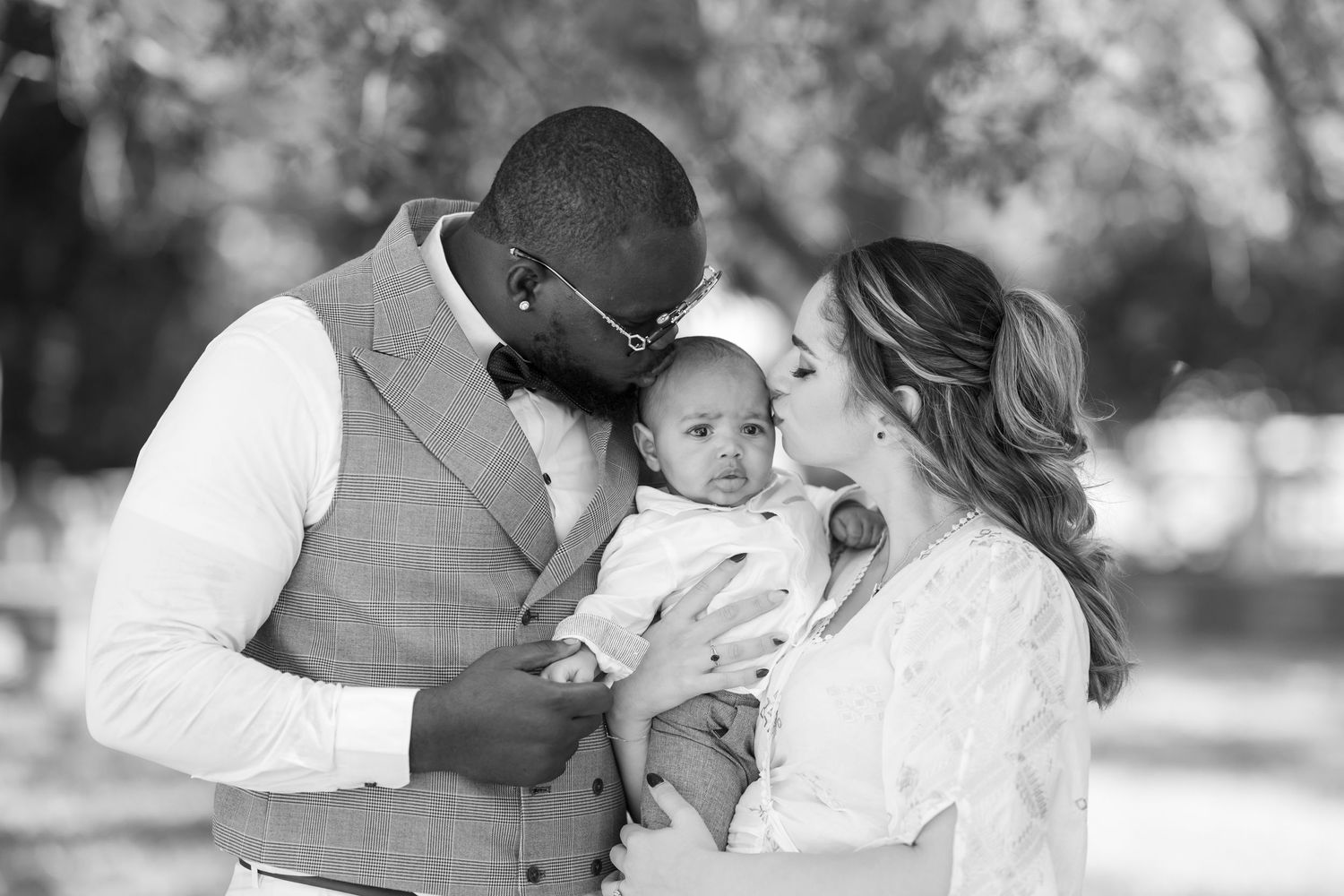 A tender family moment captured in black and white as parents share an intimate moment with their baby outdoors.