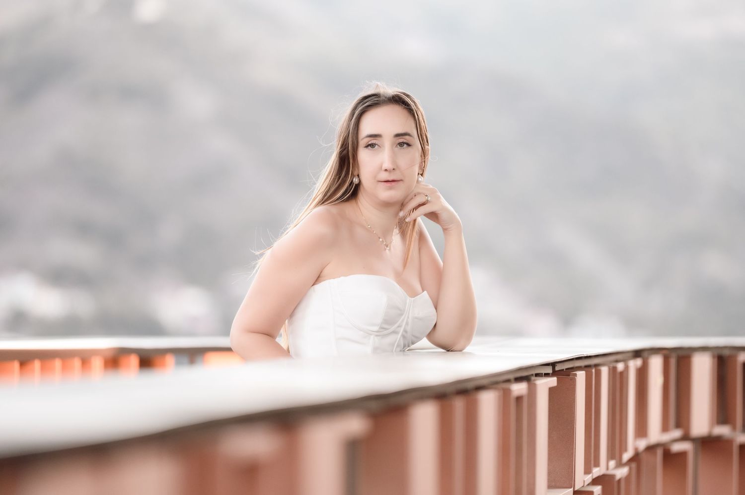 Bride in white dress posed on modern balcony with mountain backdrop.