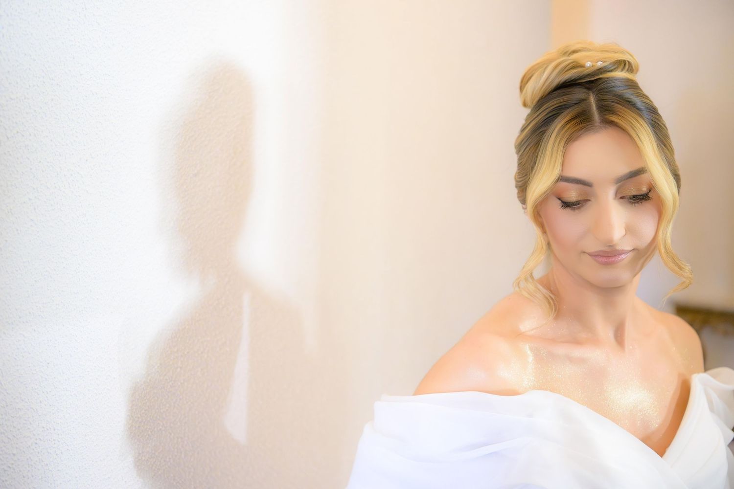 Bride with natural makeup and elegant hairstyle looks down peacefully in soft window light.