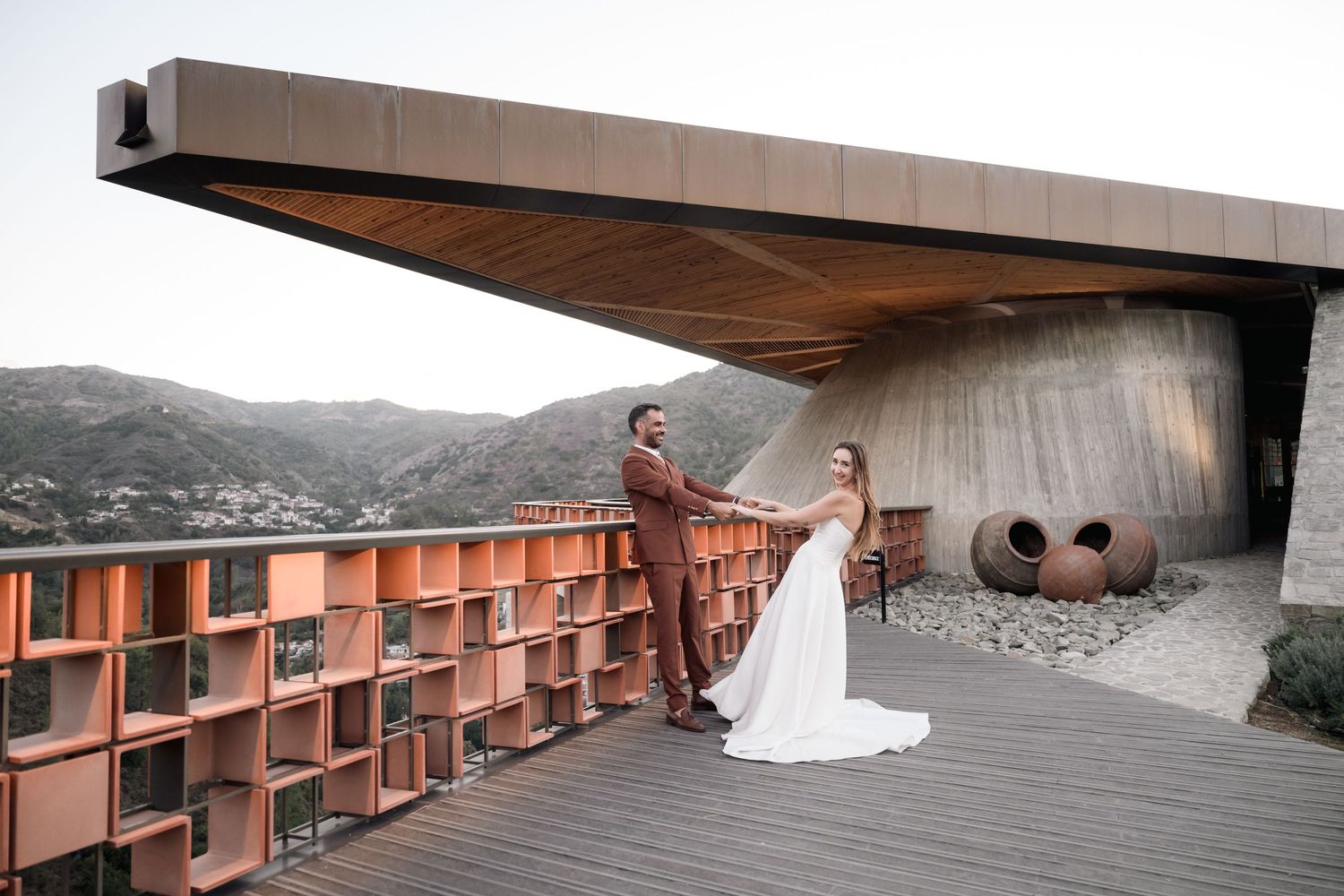 Wedding couple posed on modern architectural balcony overlooking mountain landscape.