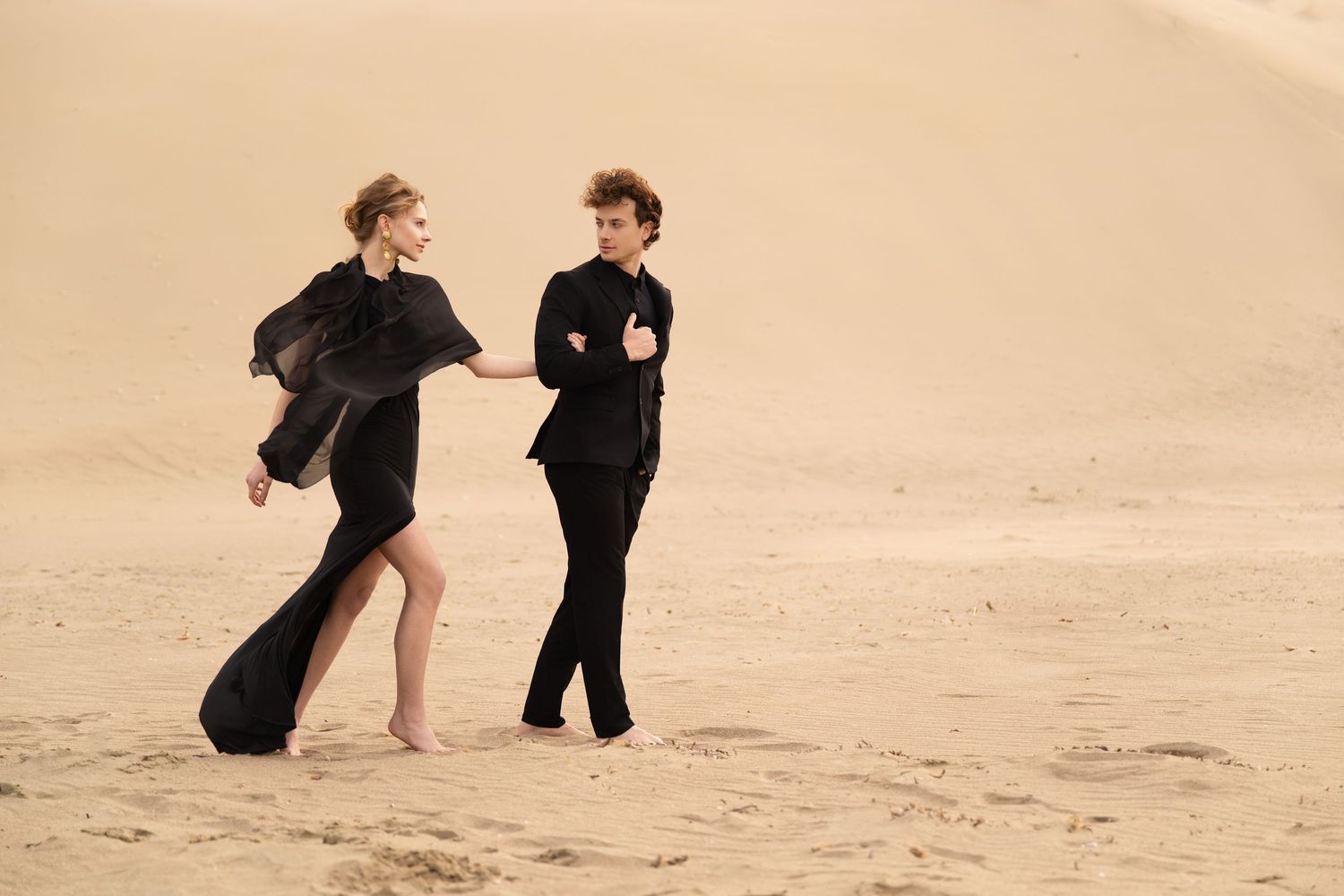 Two people in dark clothing dance together on a sandy beach at sunset.