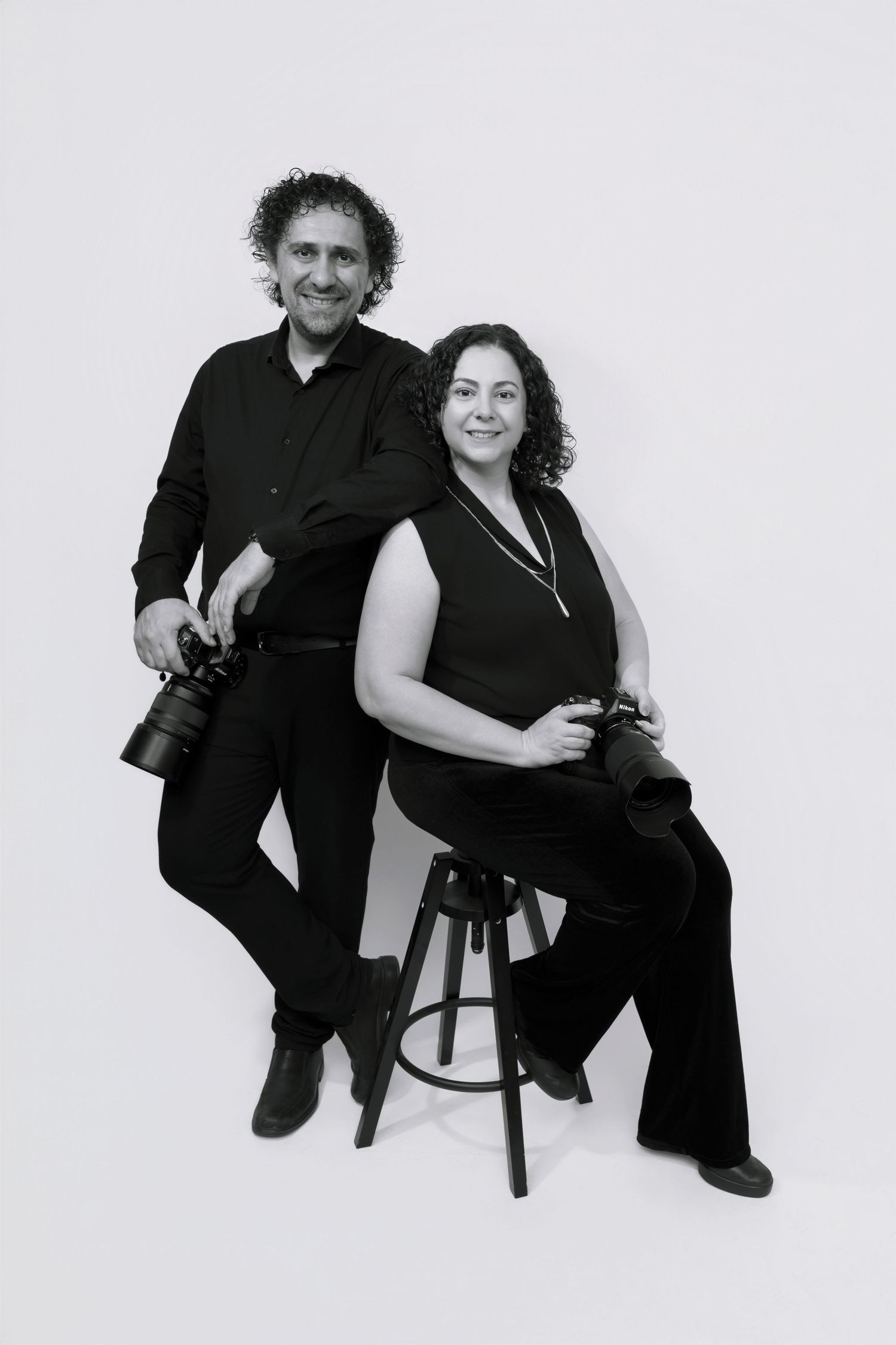 Black and white studio portrait series showing a couple in casual dark clothing posing together on a stool.