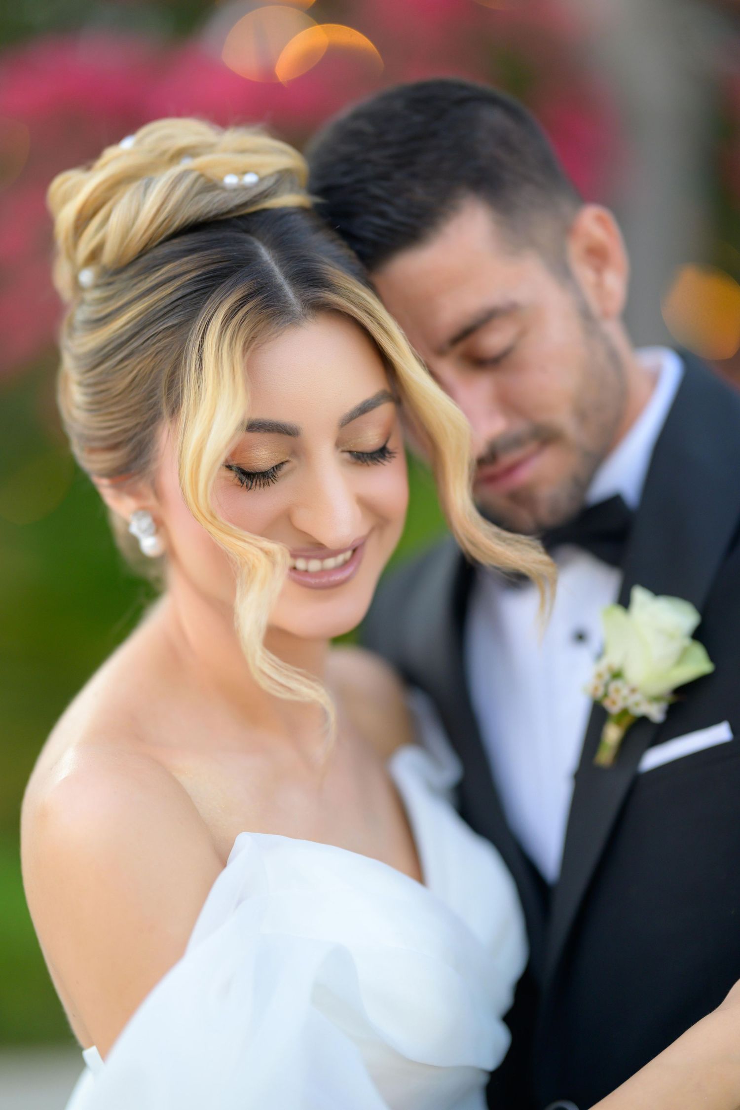 A romantic wedding portrait shows a couple in traditional formal attire embracing in front of colorful flowers.