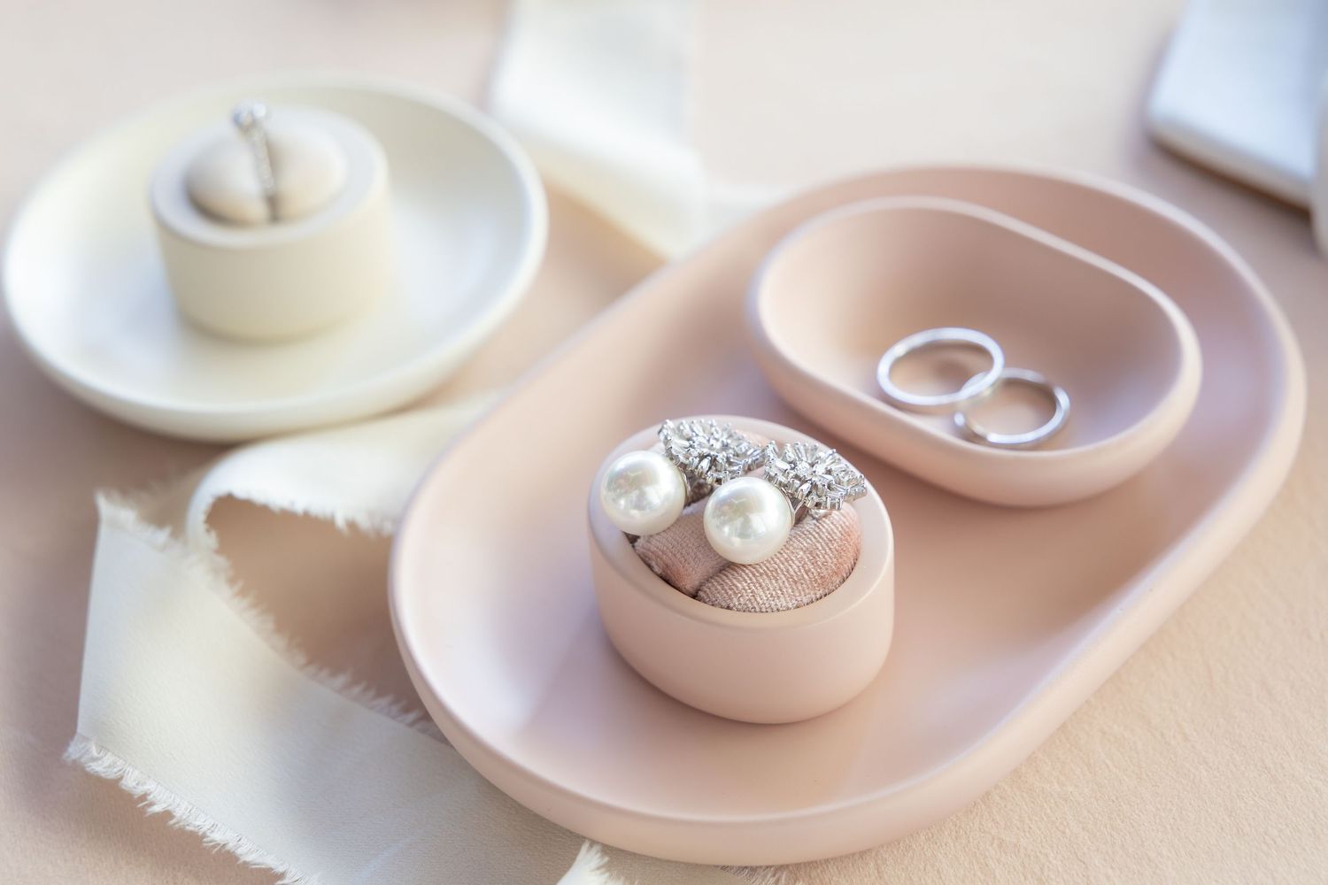 Small light pink and cream colored ring holders and trinket dishes displayed on pastel surface.