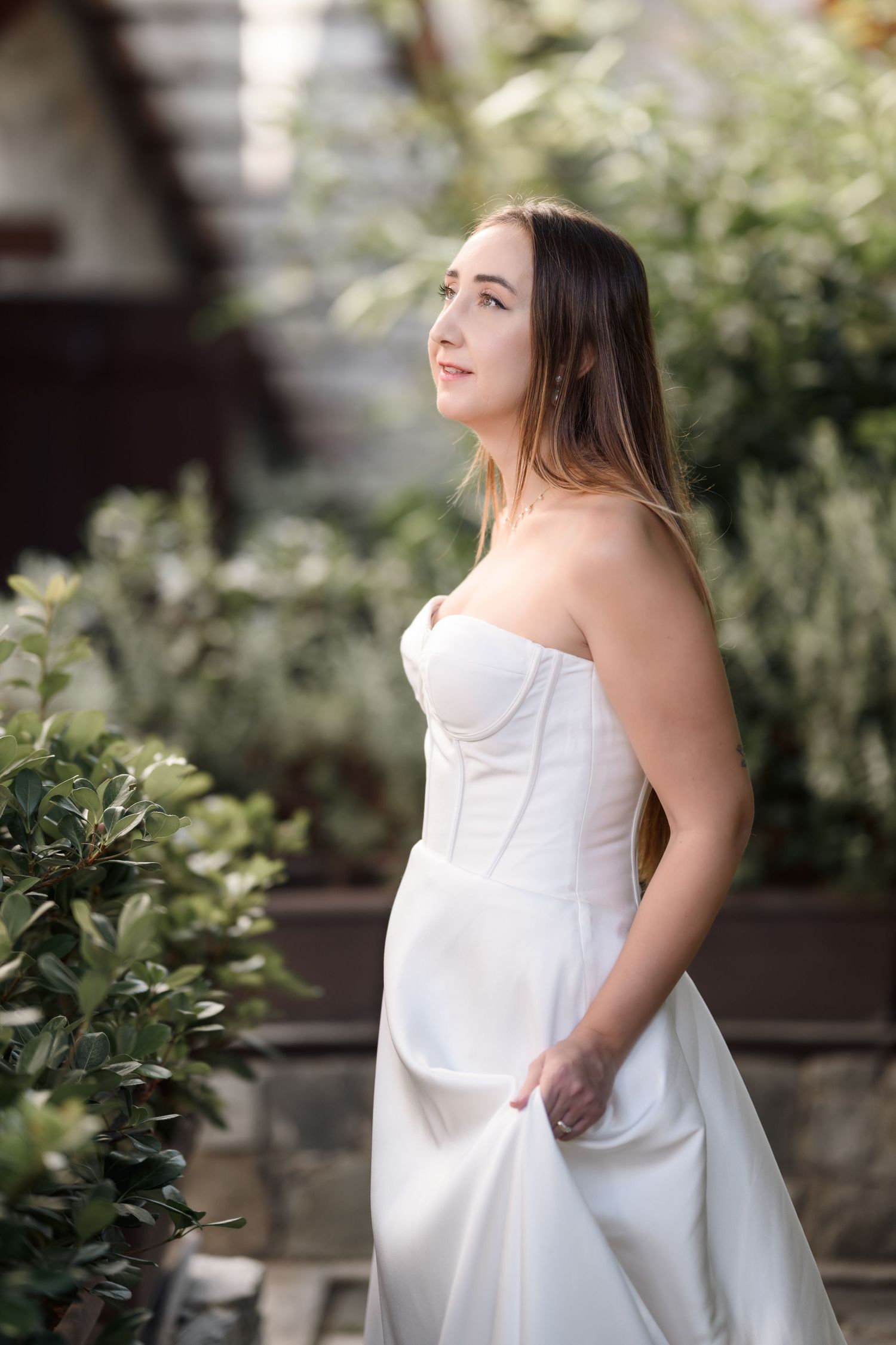 A classic white strapless wedding dress captured in a garden setting with natural greenery.