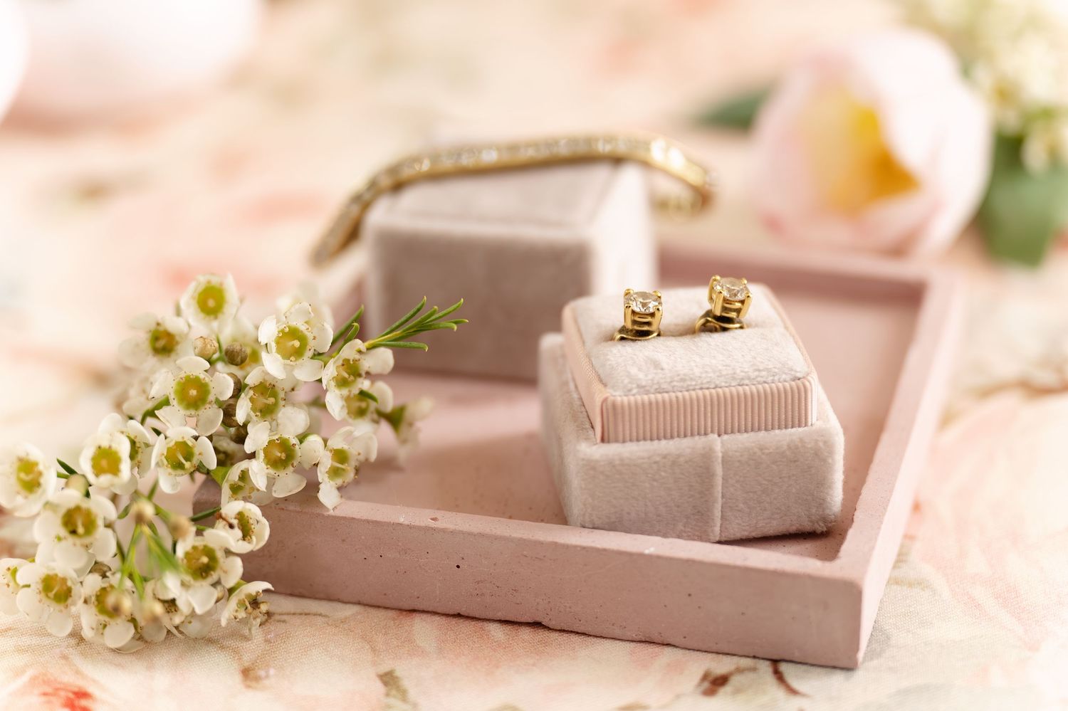 Delicate pink and white wedding accessories with earrings and floral decor arranged on elegant tray.
