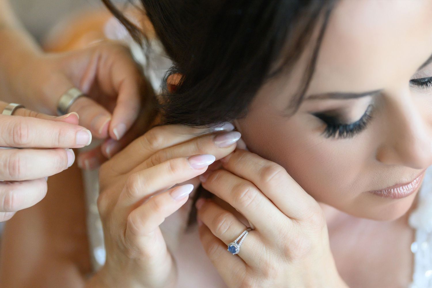 Professional makeup artist applying delicate final touches to bride's eye makeup and earrings.