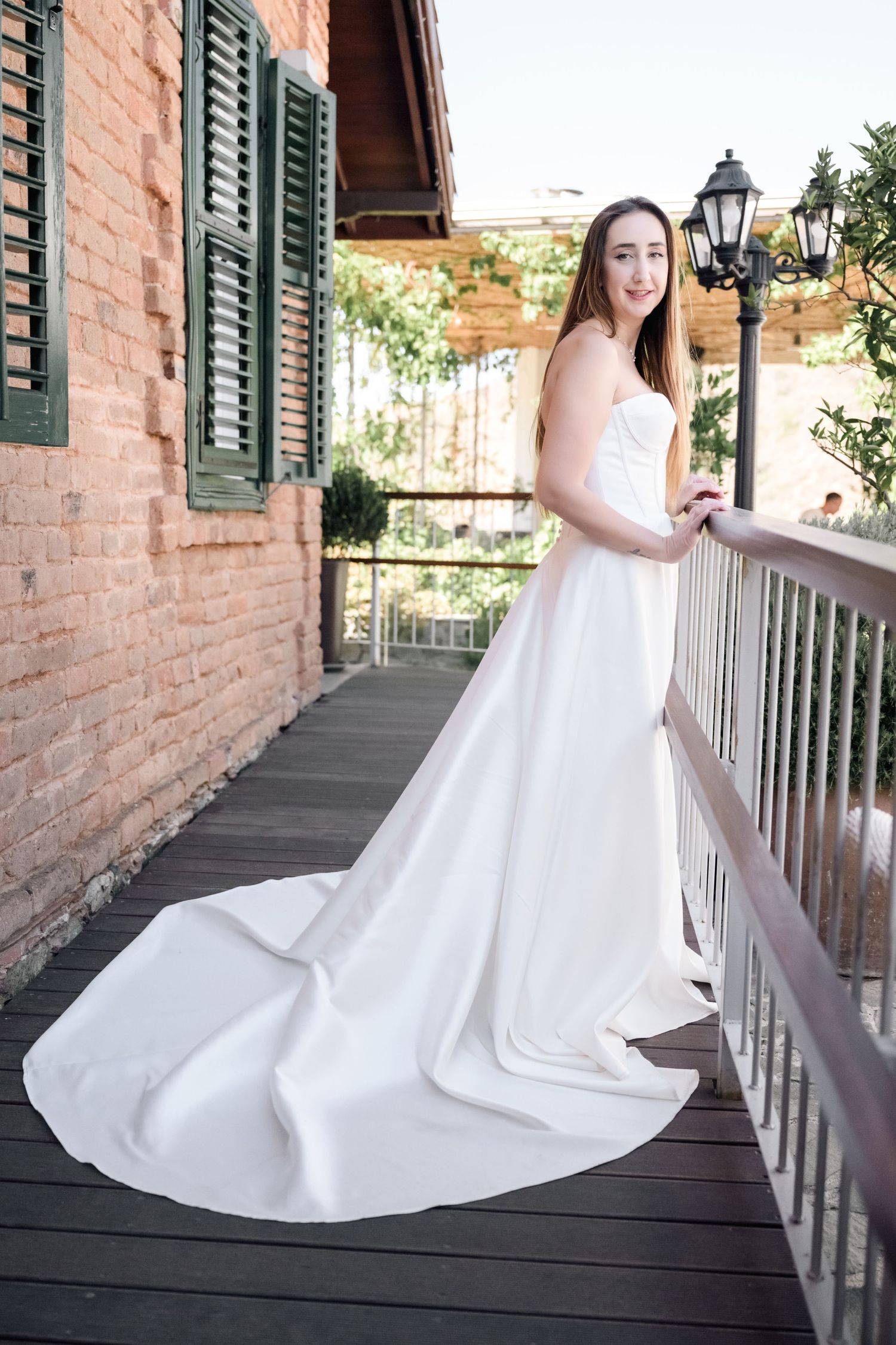 Bride in flowing white gown poses on vintage brick building's wooden porch.