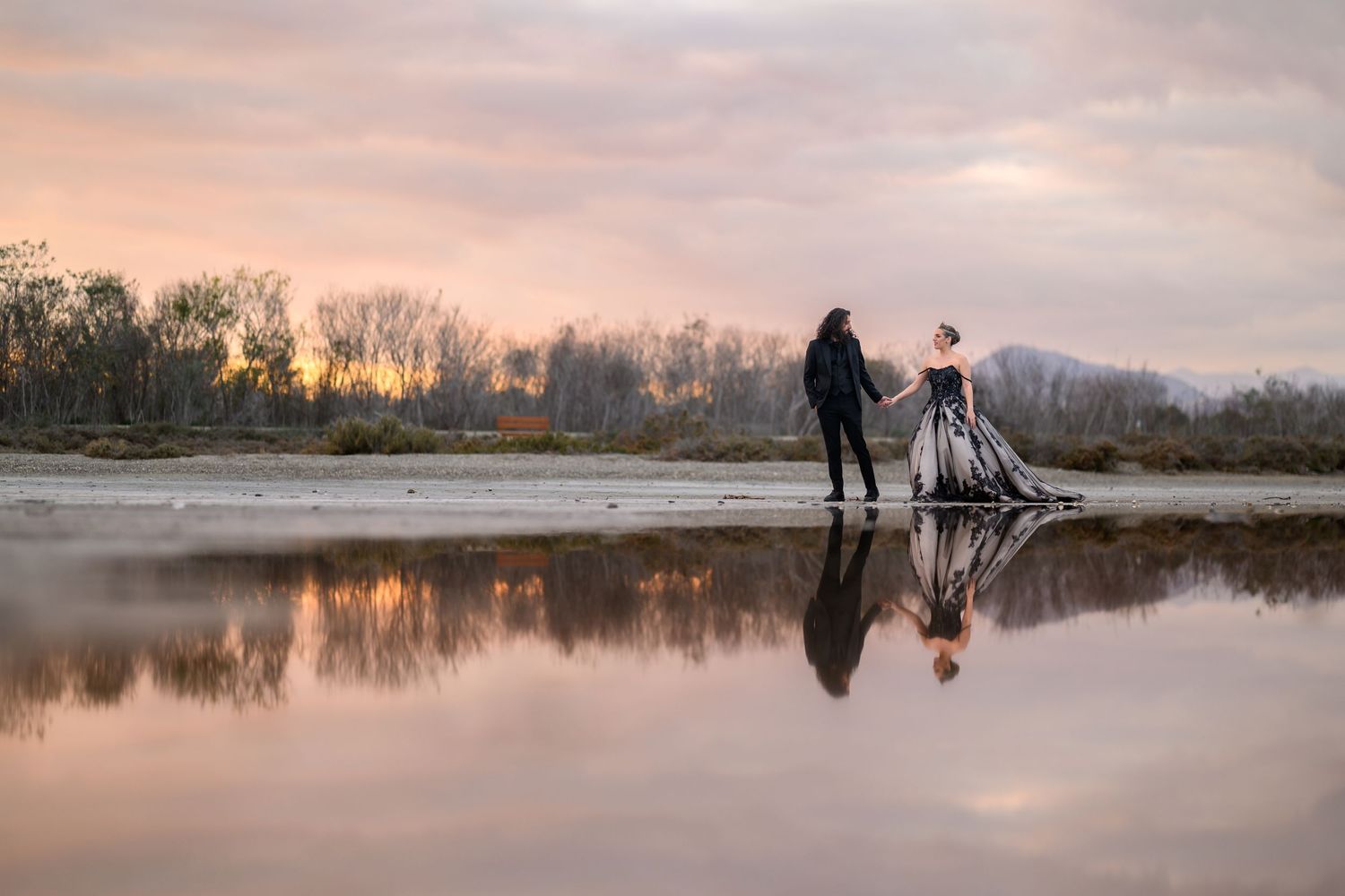Silhouettes of a couple standing by a lake at sunset with reflections in the calm water.