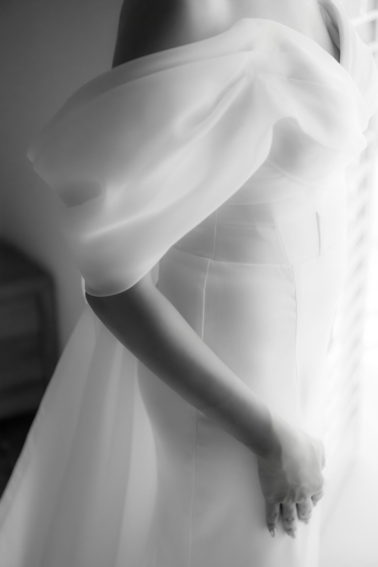 Close-up details of flowing white wedding dress fabric creating soft, ethereal folds in black and white photography.