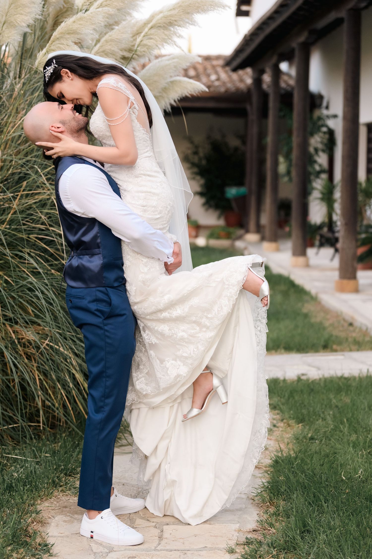 A romantic dip pose between newlyweds in a garden setting with the bride in a white lace gown and groom in navy suit.