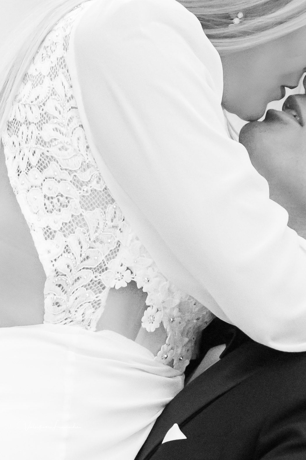 Black and white close-up of lace detail on wedding dress during intimate moment.